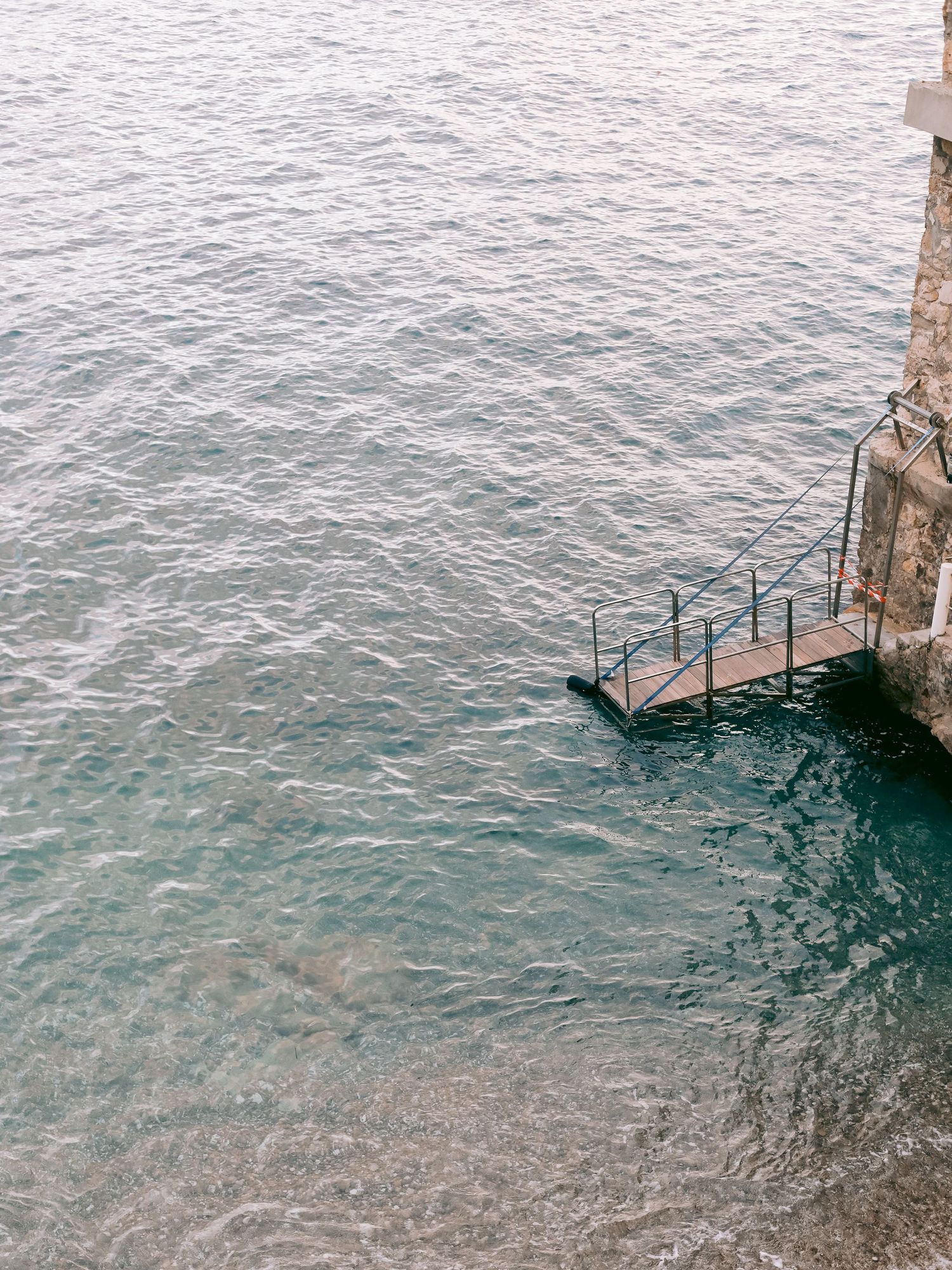 Crystal clear Mediterranean waters lapping against stone walls along the coastline.