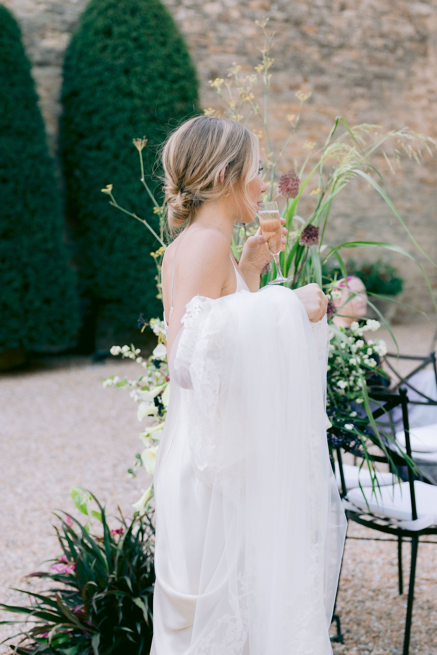 Bride in flowing white dress with floral arrangements in outdoor garden setting.