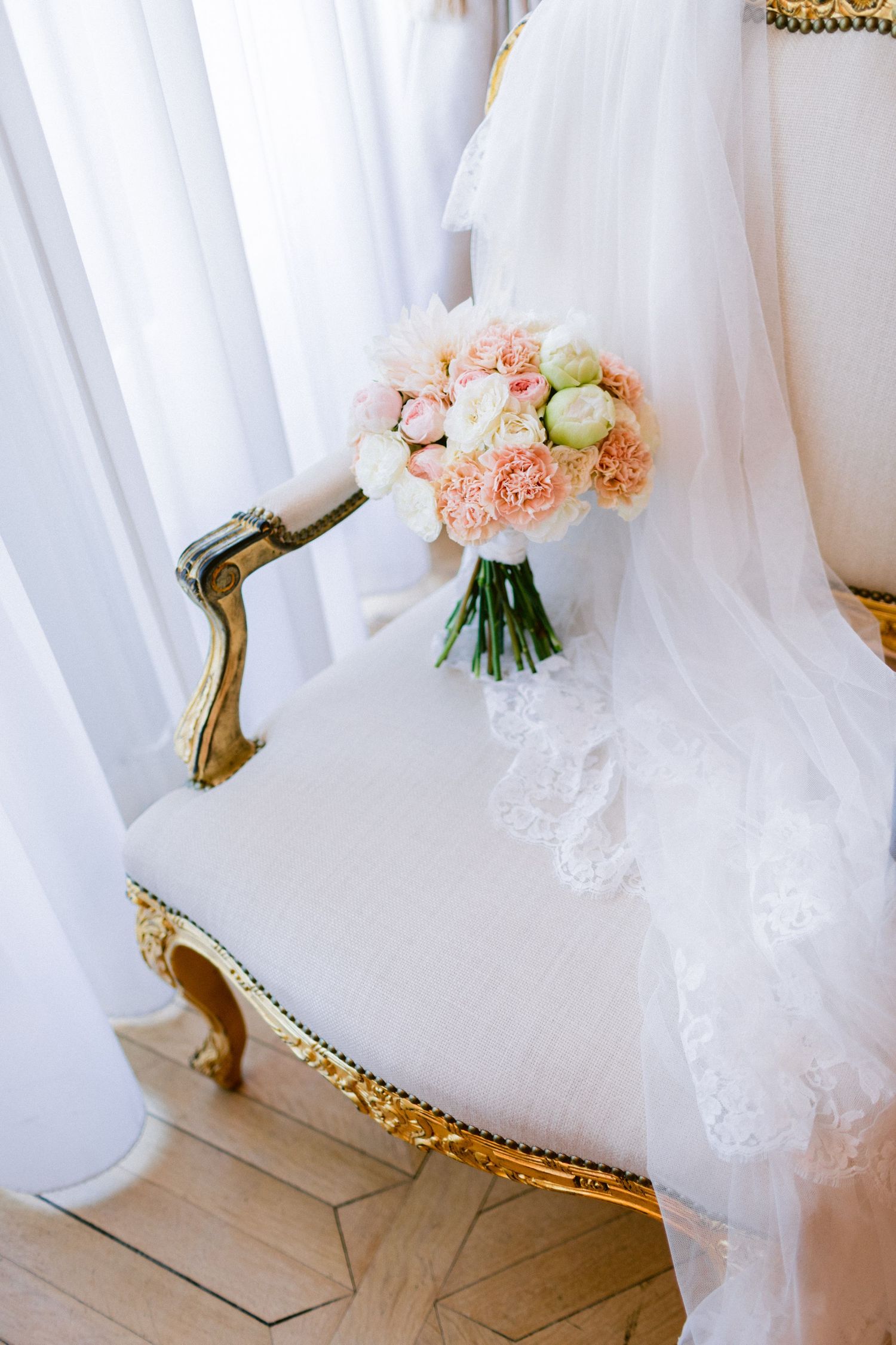 Pink and white bridal bouquet resting on flowing white wedding dress fabric.