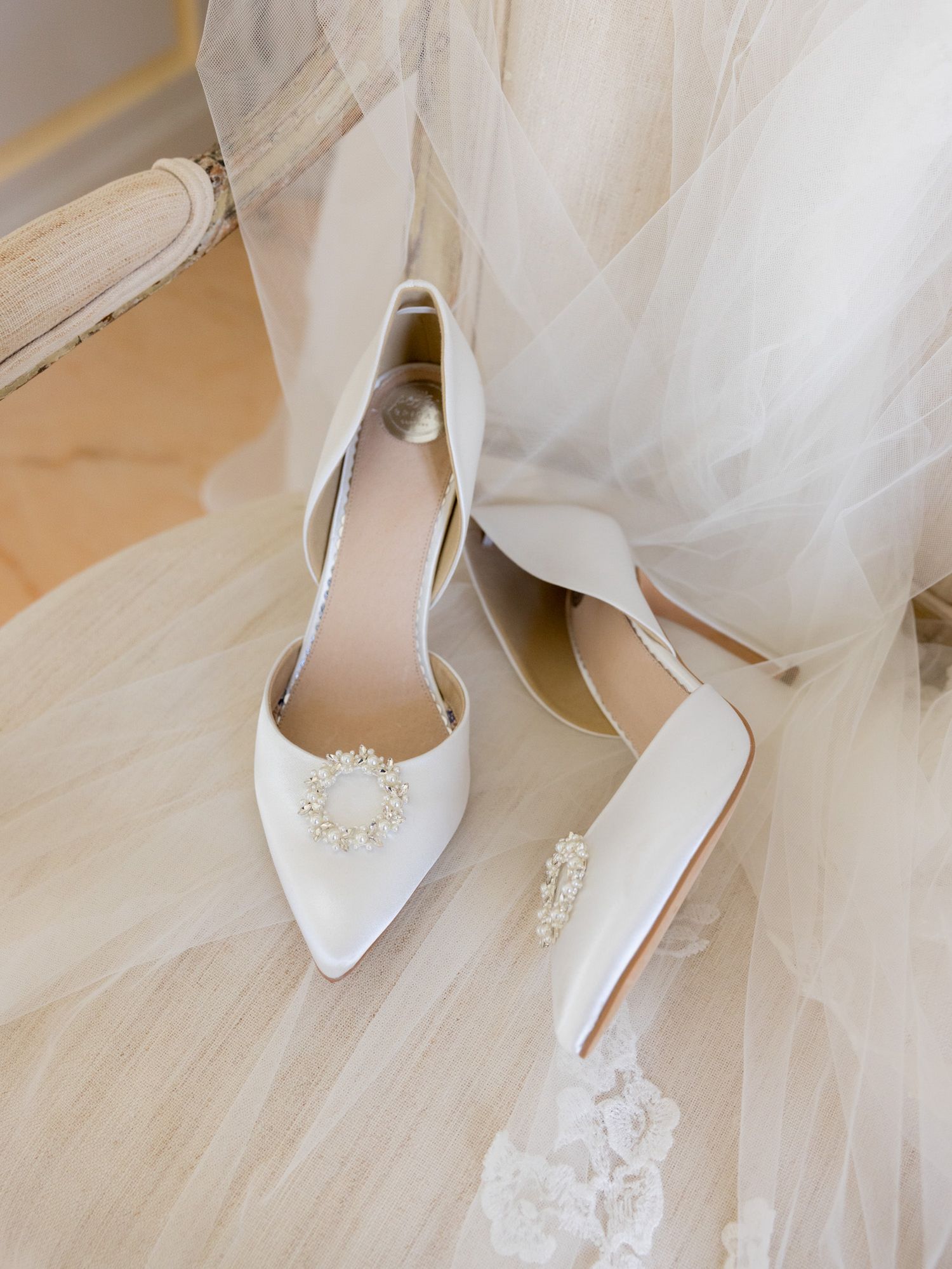 Elegant white bridal shoes with crystal embellishments against tulle fabric.
