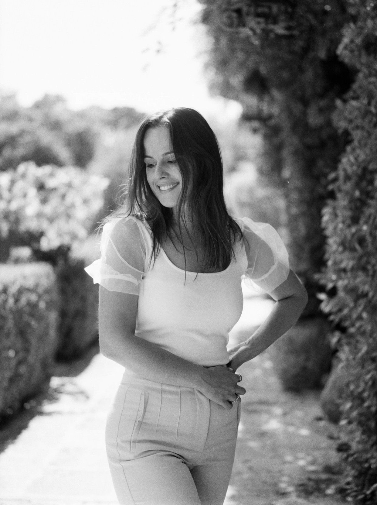 Woman in white dress smiling and posing outdoors in a natural black and white portrait series.