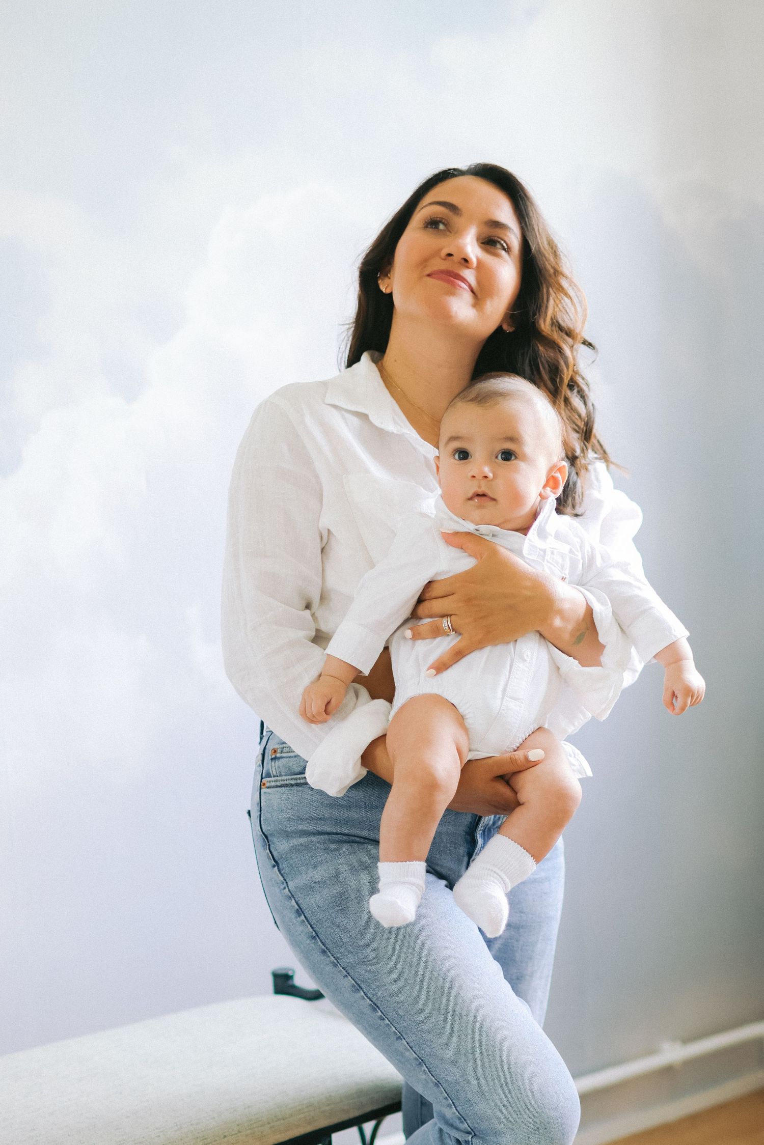 Parent holding baby in white outfit against white wall.