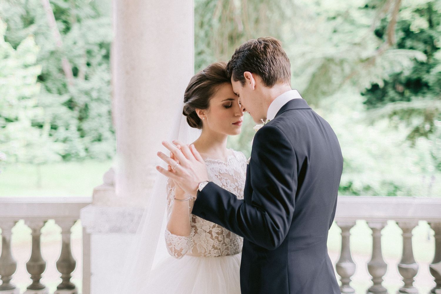 Romantic wedding couple sharing an intimate moment on an elegant stone balcony.