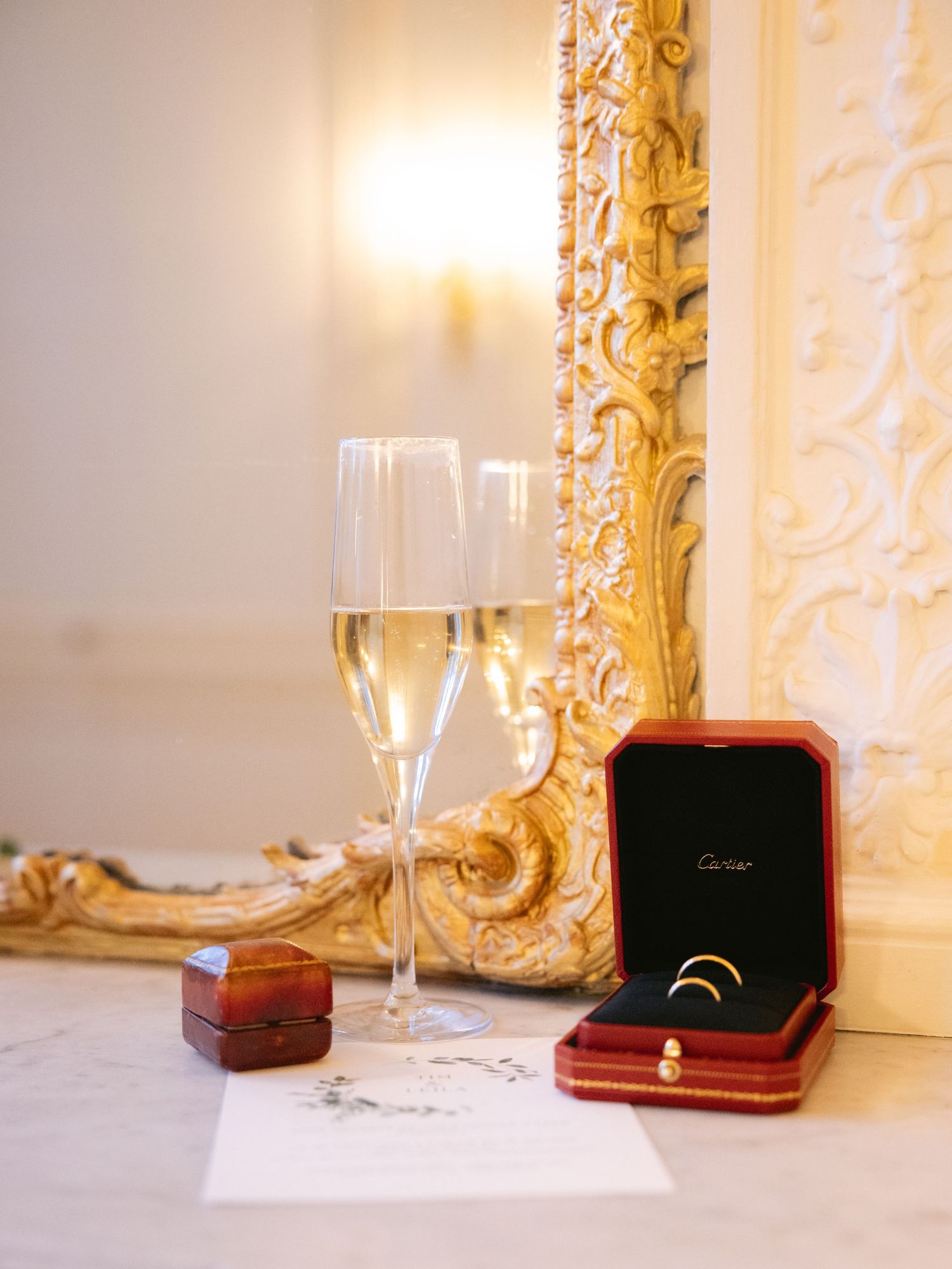 Wedding rings in a red velvet box displayed next to champagne glasses.