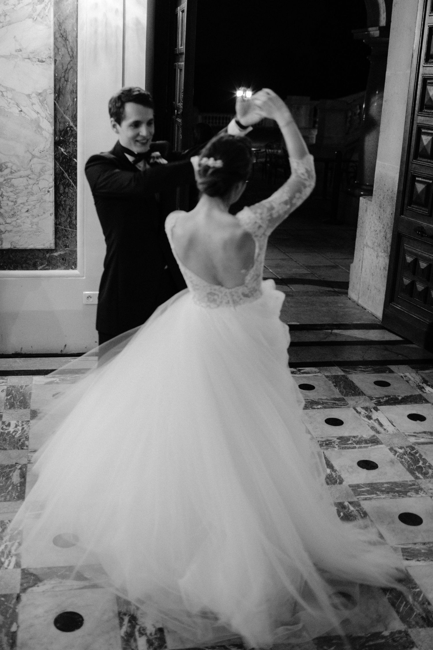 A person in a flowing white wedding dress twirls and dances across a tiled floor.