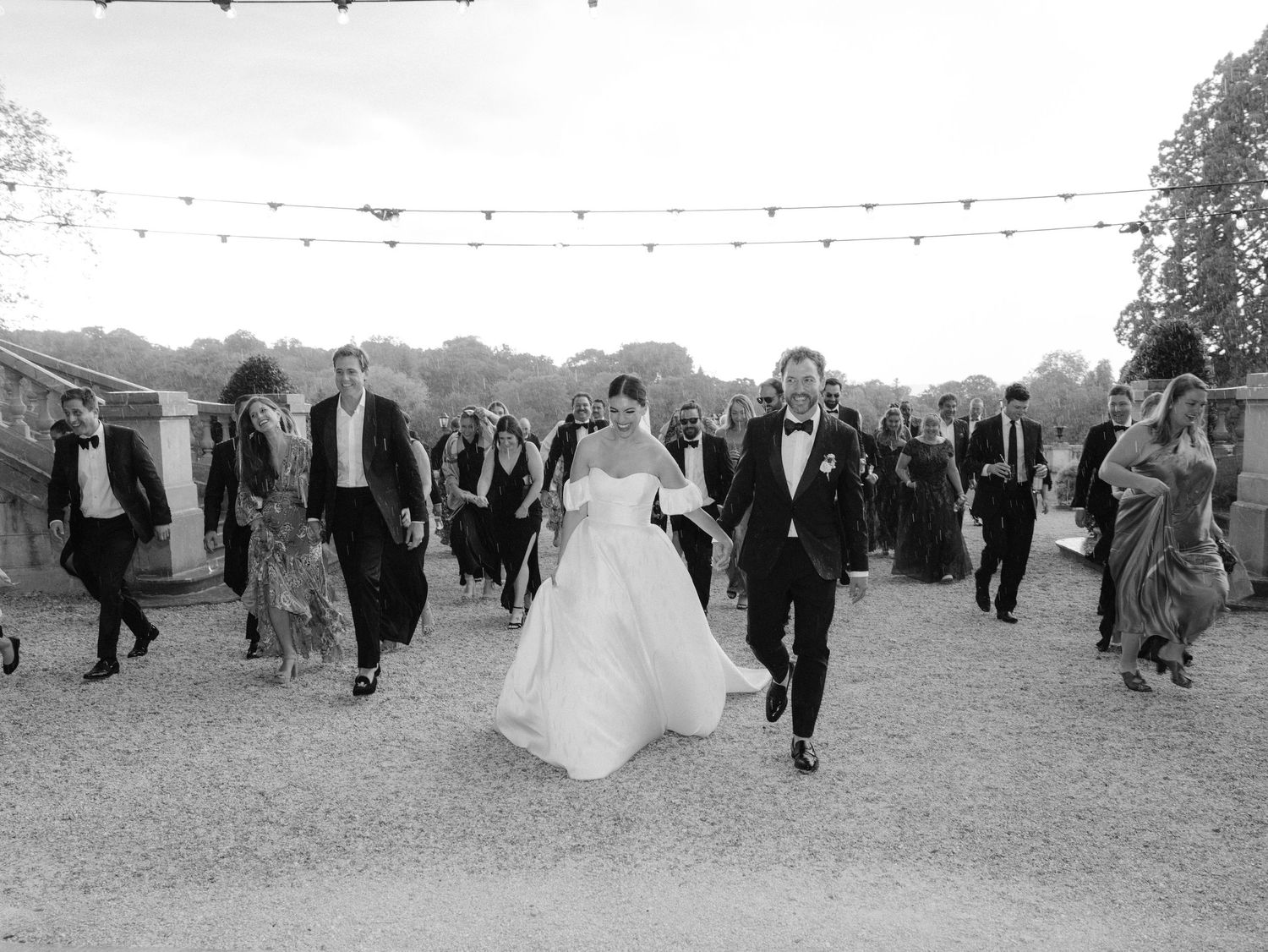 Black and white photo of wedding guests dancing and celebrating outdoors.