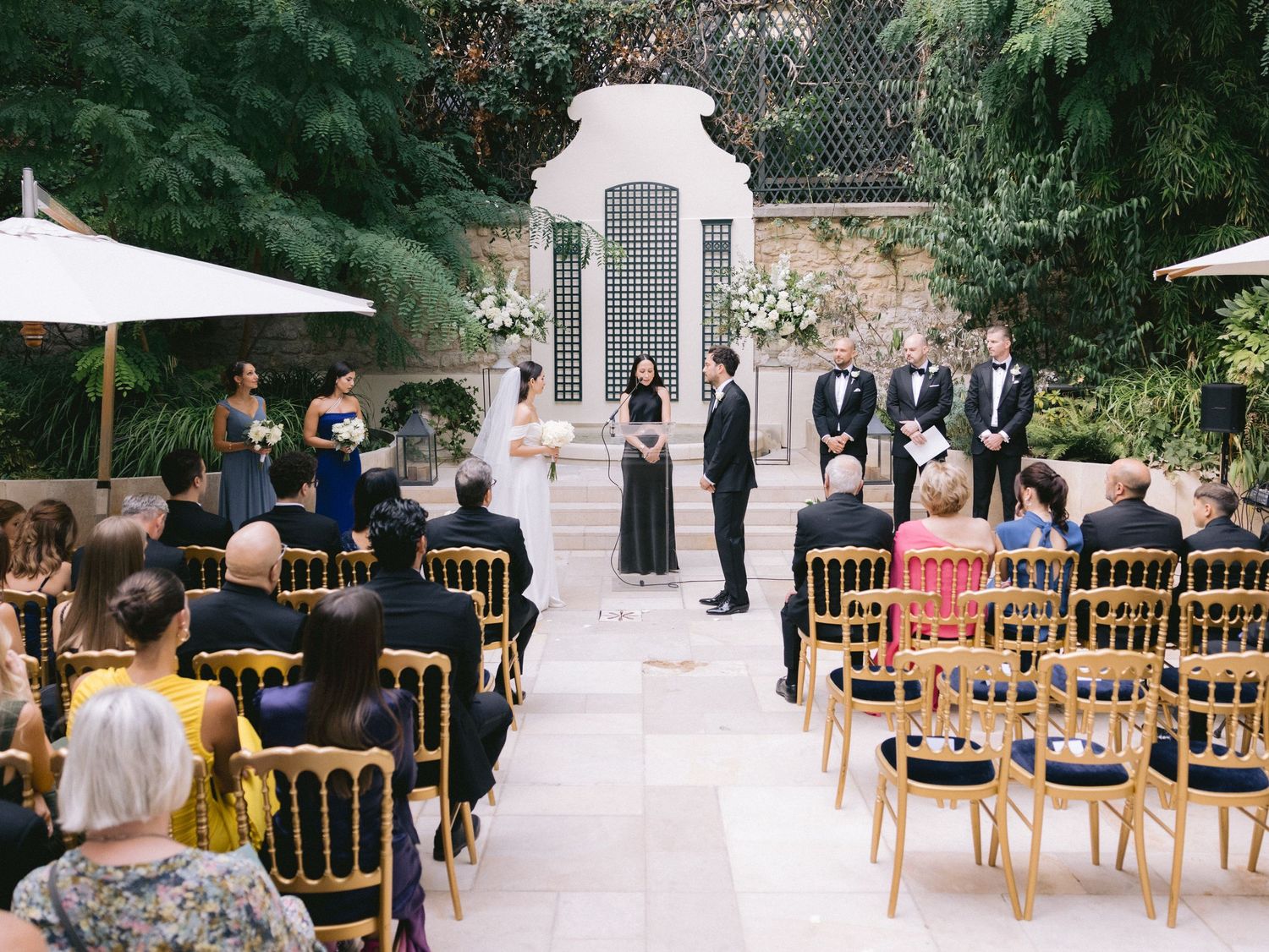 Garden wedding ceremony venue with gold chairs arranged in rows surrounded by greenery.