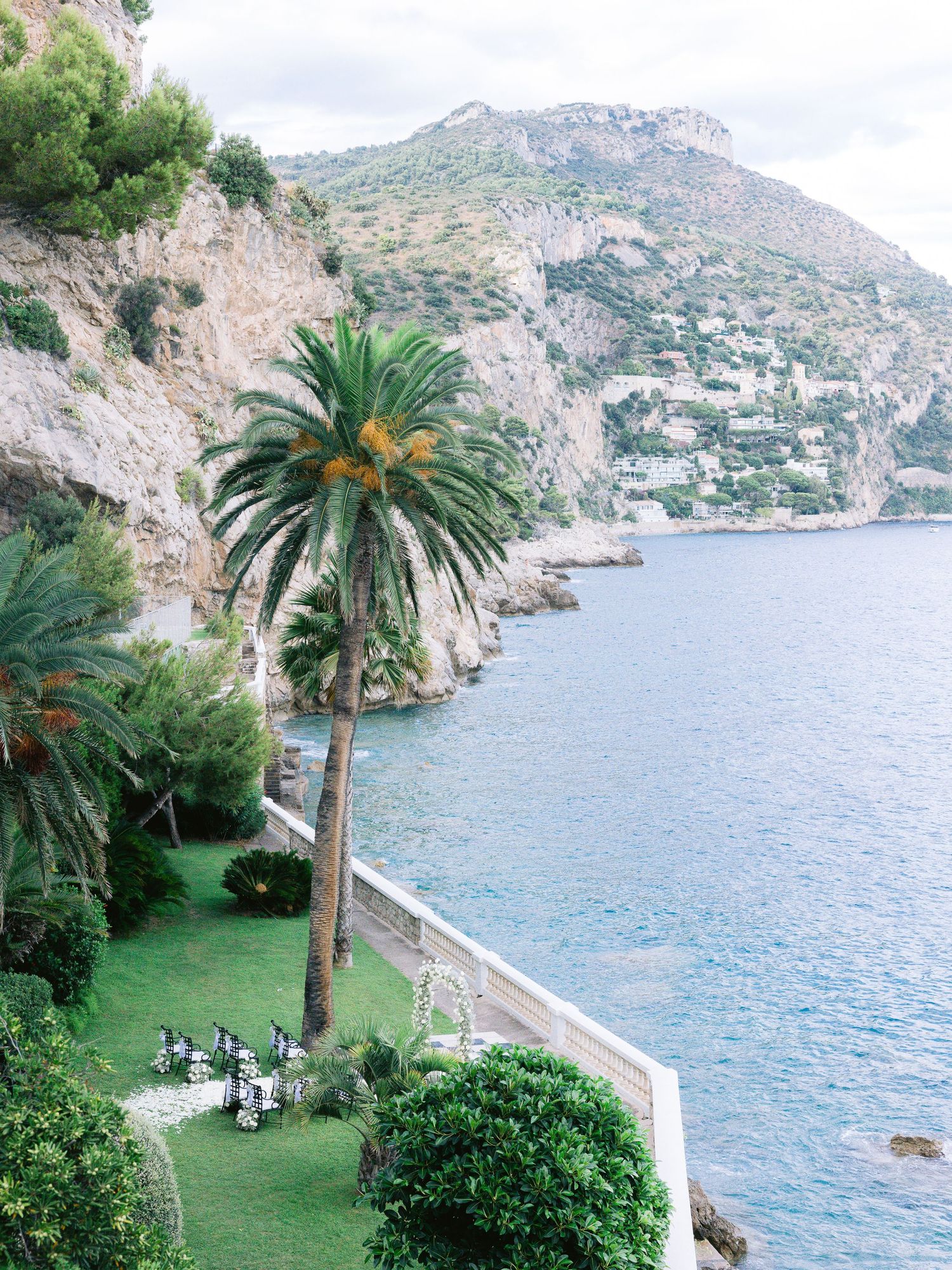 Scenic coastal garden with palm trees and manicured lawns overlooking the Mediterranean bay.