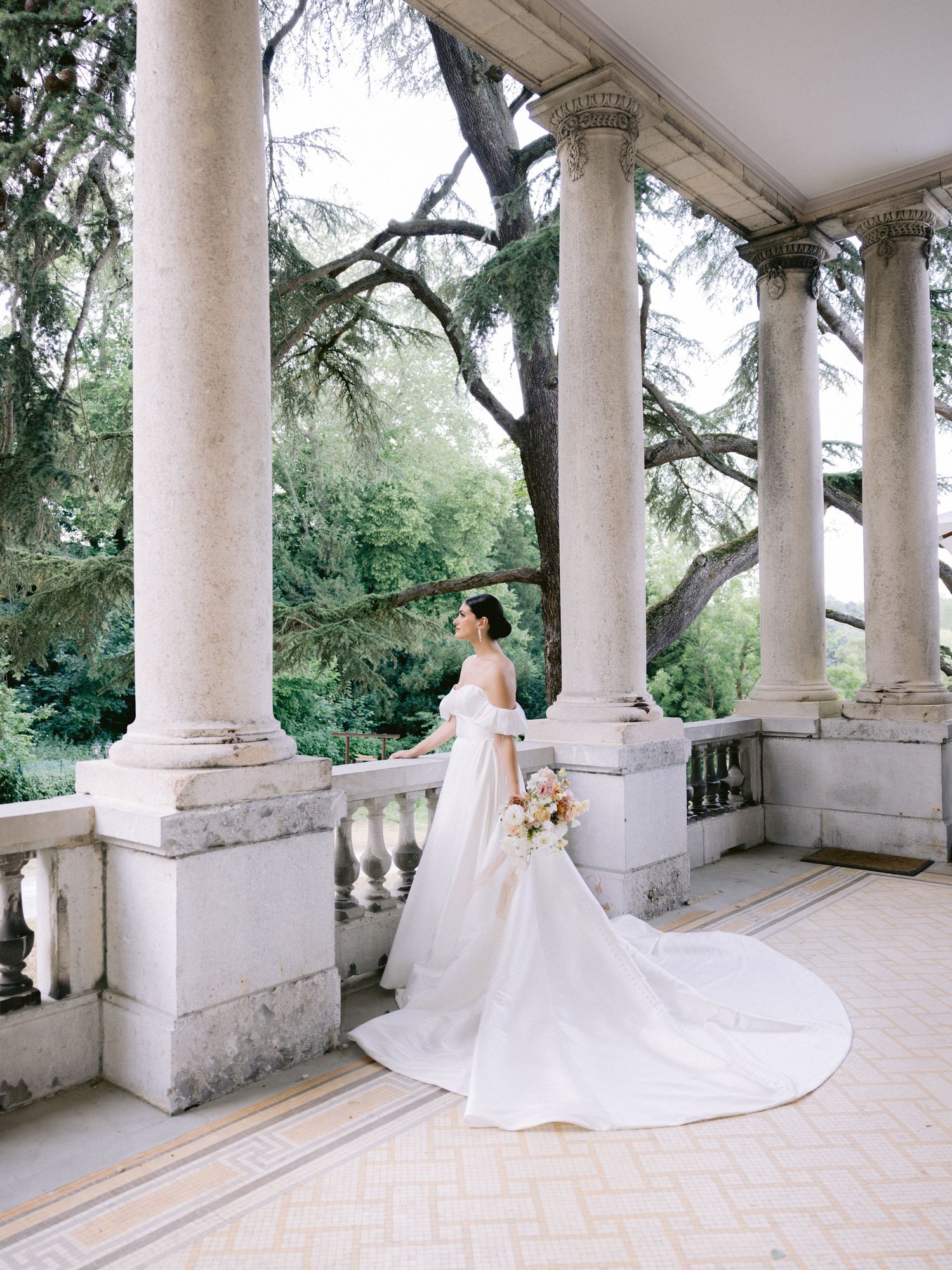 Elegant bridal portrait on columned terrace with flowing white gown and bouquet.