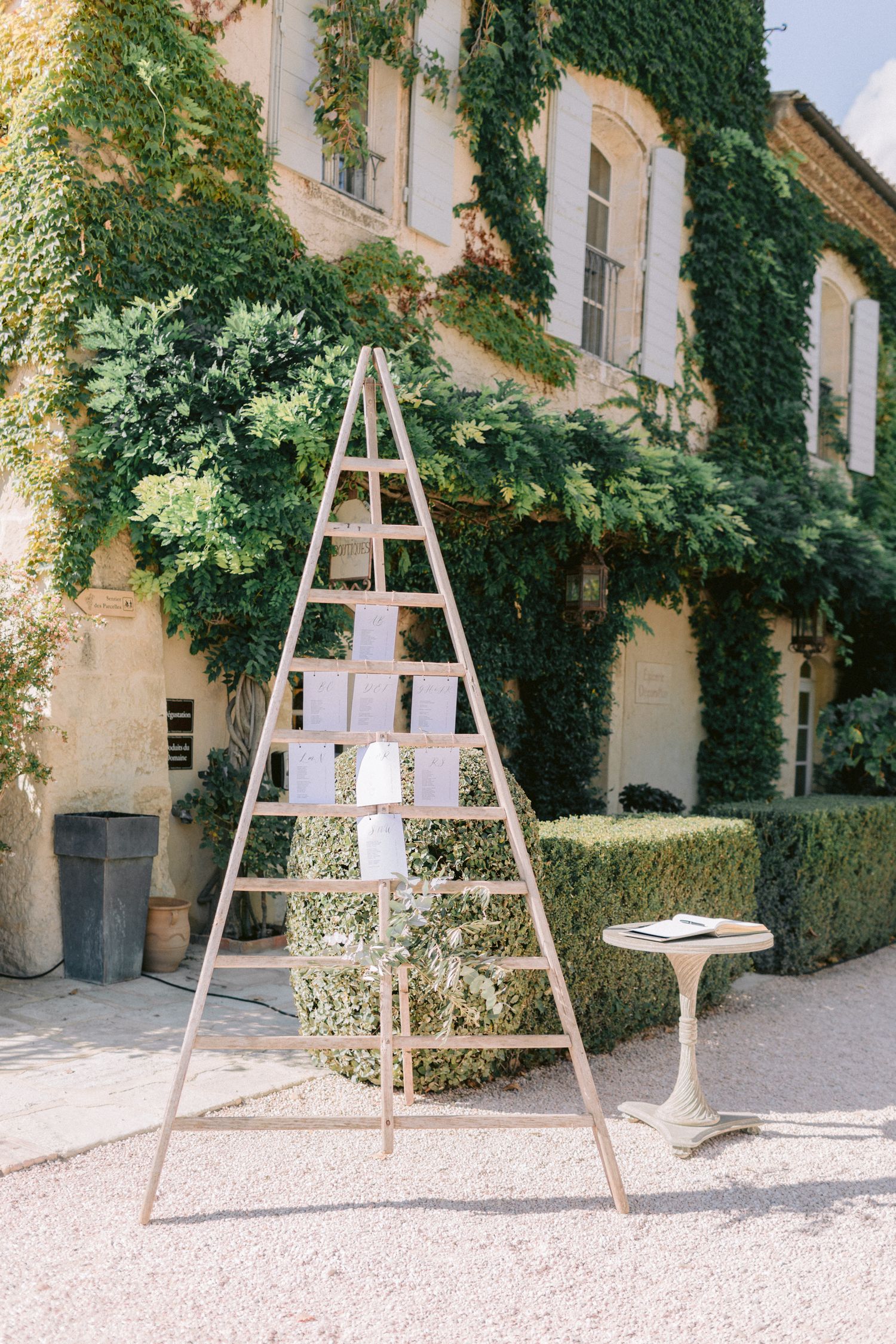 Wooden ladder display with hanging frames against an ivy-covered building facade.