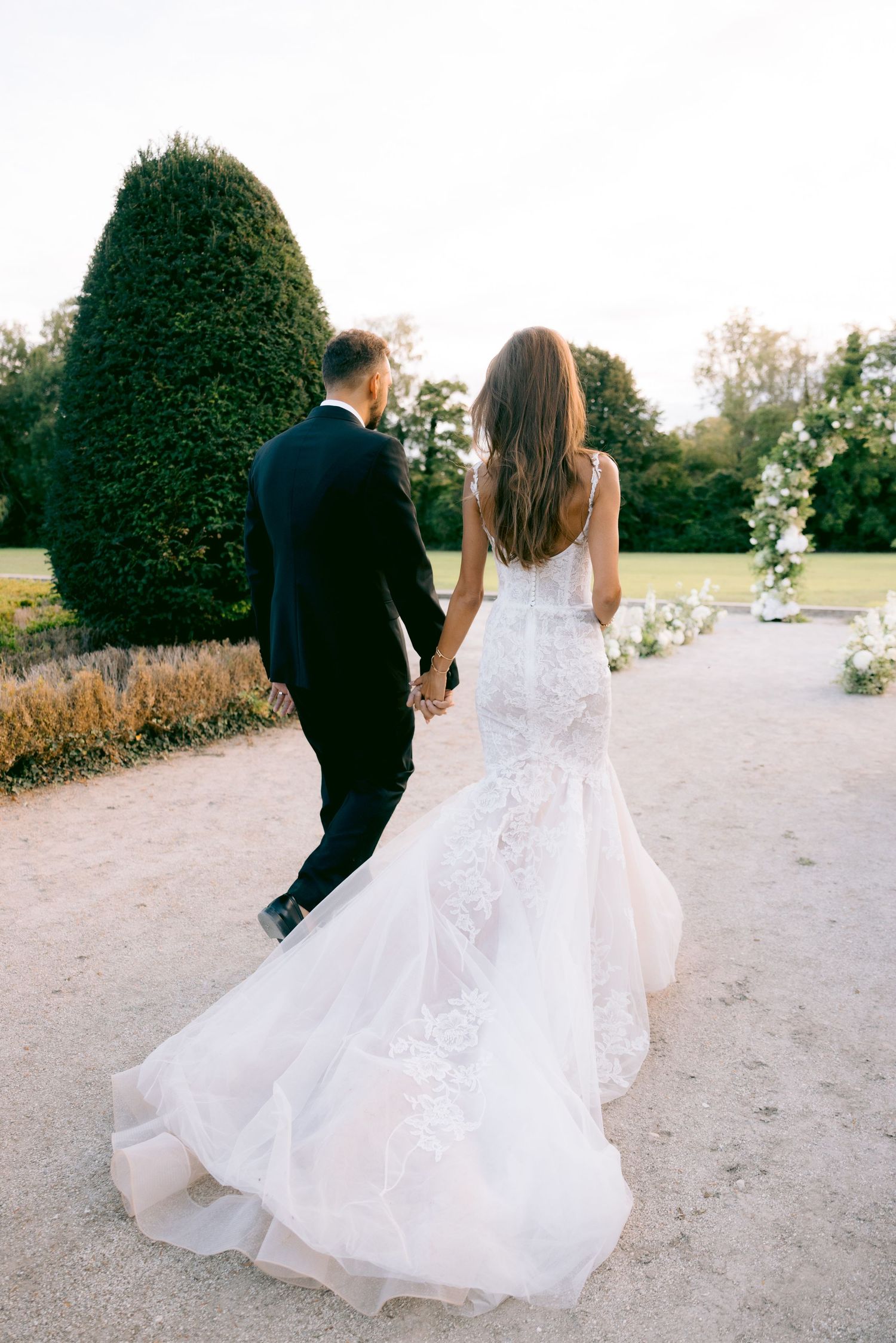 Newlyweds walking along garden path with flowing white wedding dress.