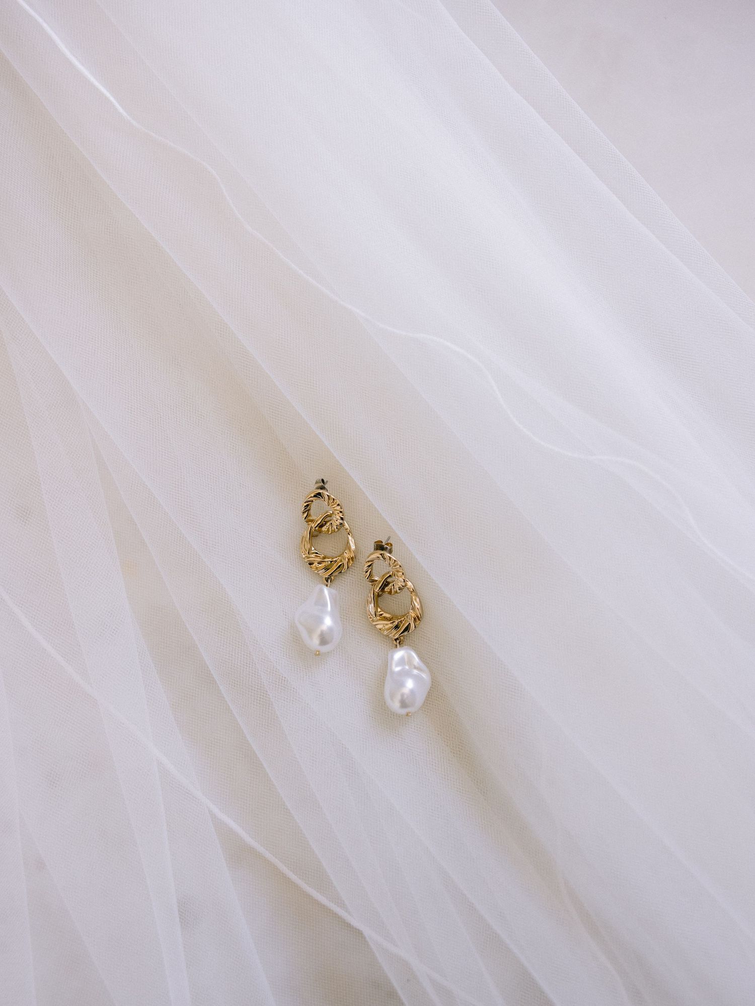 Delicate gold and pearl bridal earrings displayed on white fabric.