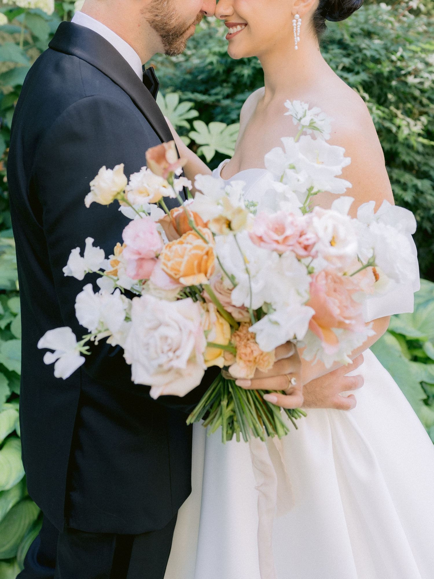 Elegant bridal bouquet featuring soft pink and white roses held between couple in formal wedding attire.