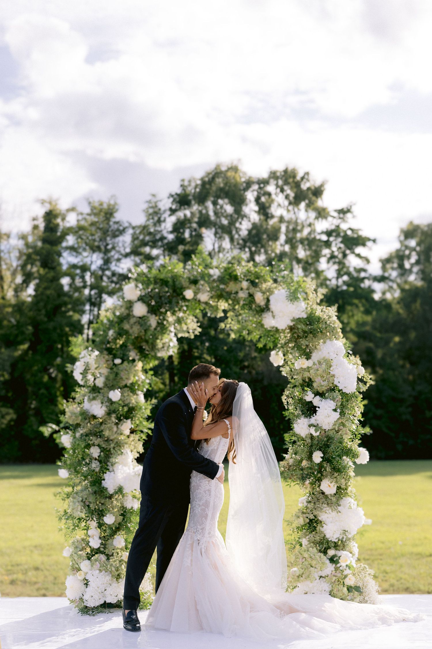 Romantic wedding ceremony under a floral arch with white roses and greenery.