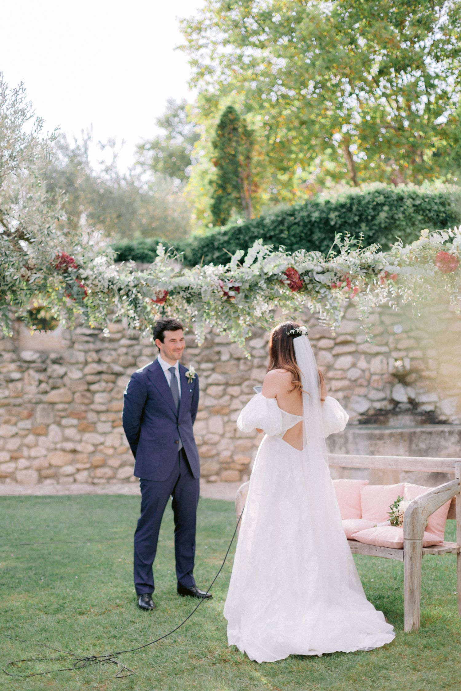 Candid wedding moments photographed in a garden setting with stone wall and natural landscaping.
