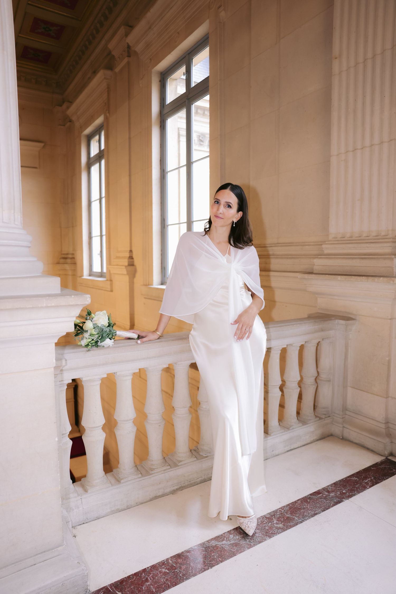 Bride portrait photograpA bride in a white dress poses elegantly against ornate marble columns and balustrades in a grand historic building.
