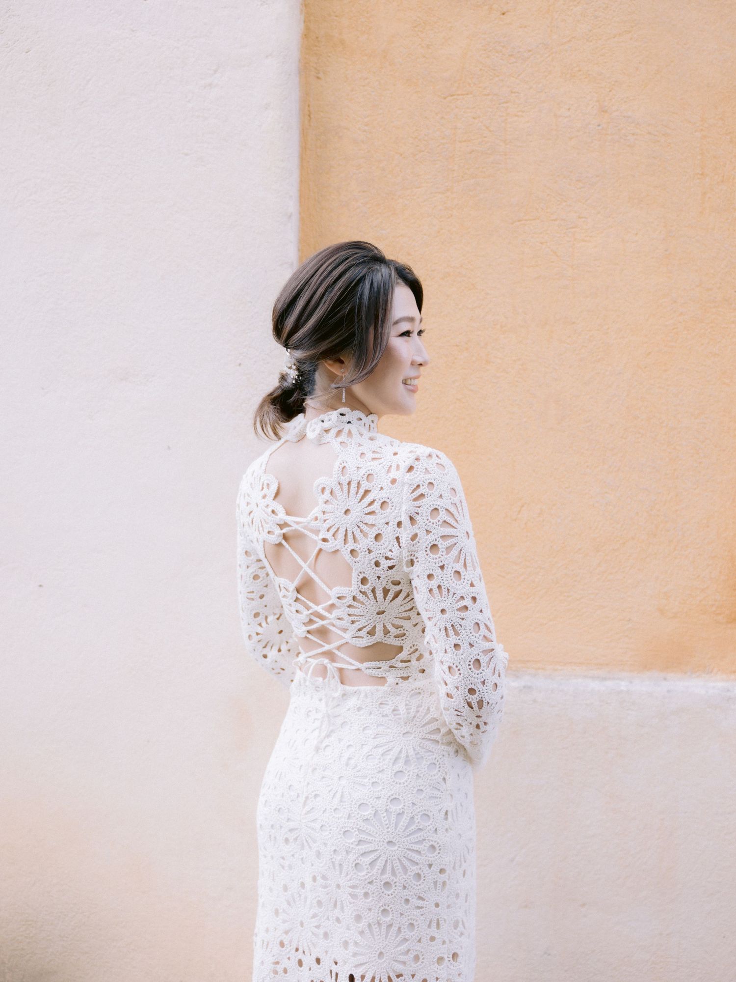 A series of four photos showing someone wearing a delicate white lace dress against a beige wall.