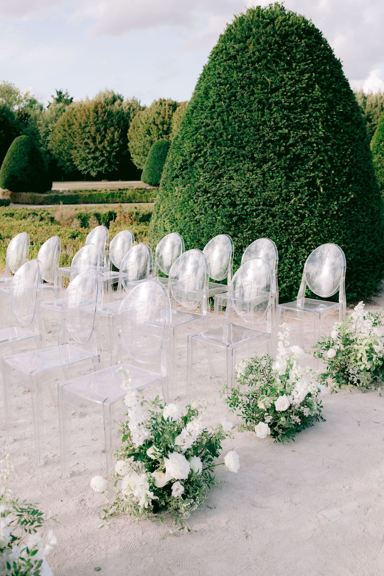 Modern outdoor wedding ceremony setup at Château de Sept Saulx with ghost chairs and floral arrangements.