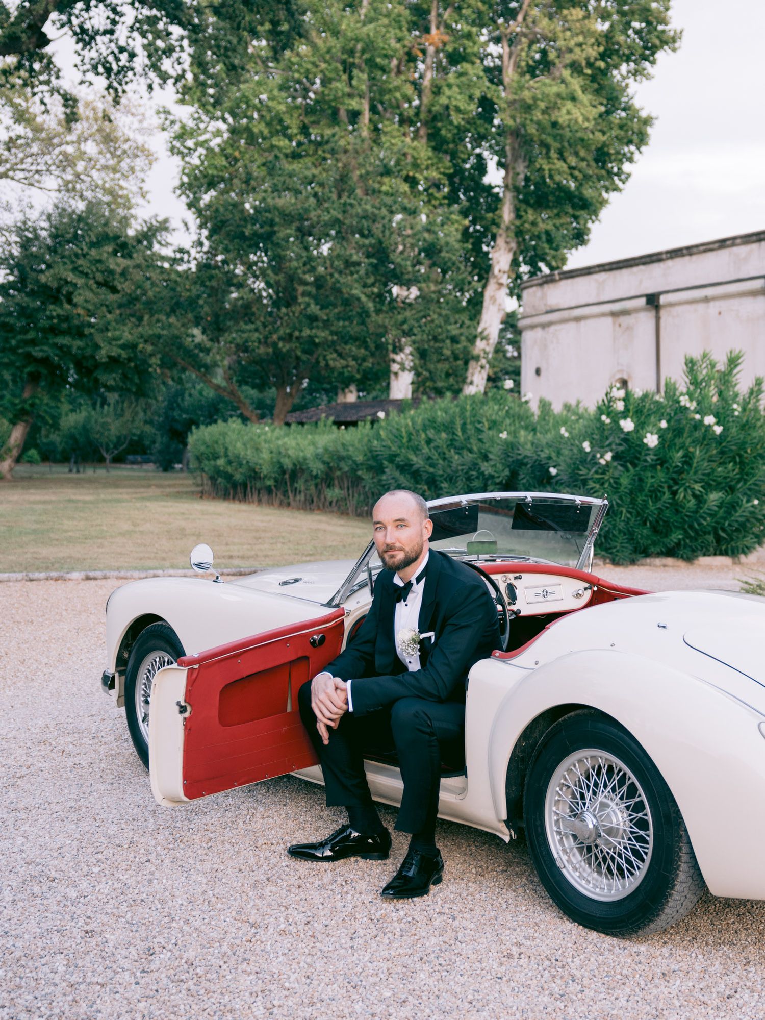 A classic red and white vintage sports car photographed in an outdoor setting.