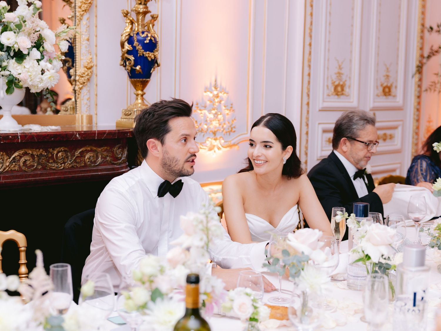 Wedding reception dining tables decorated with elegant centerpieces and fine china in an ornate ballroom.