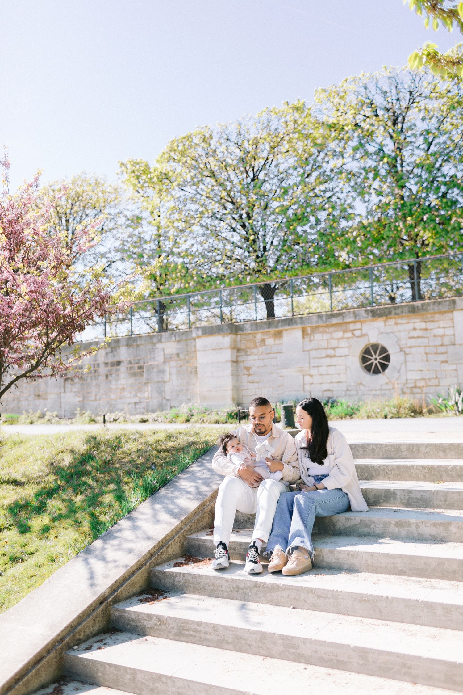 Family relaxing on stone steps outdoors with blooming cherry trees in background.