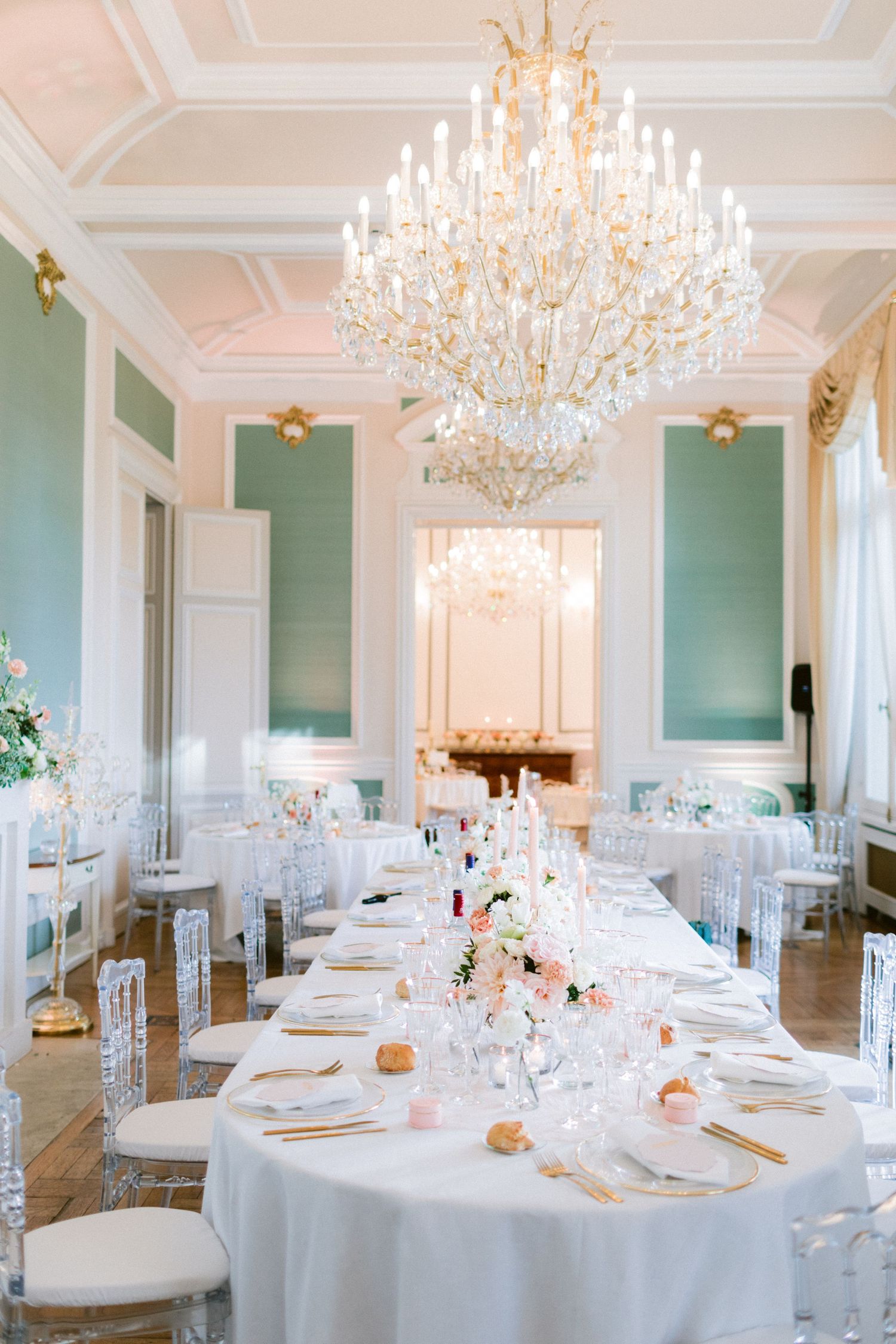 Luxurious wedding reception room with crystal chandeliers and white table settings.