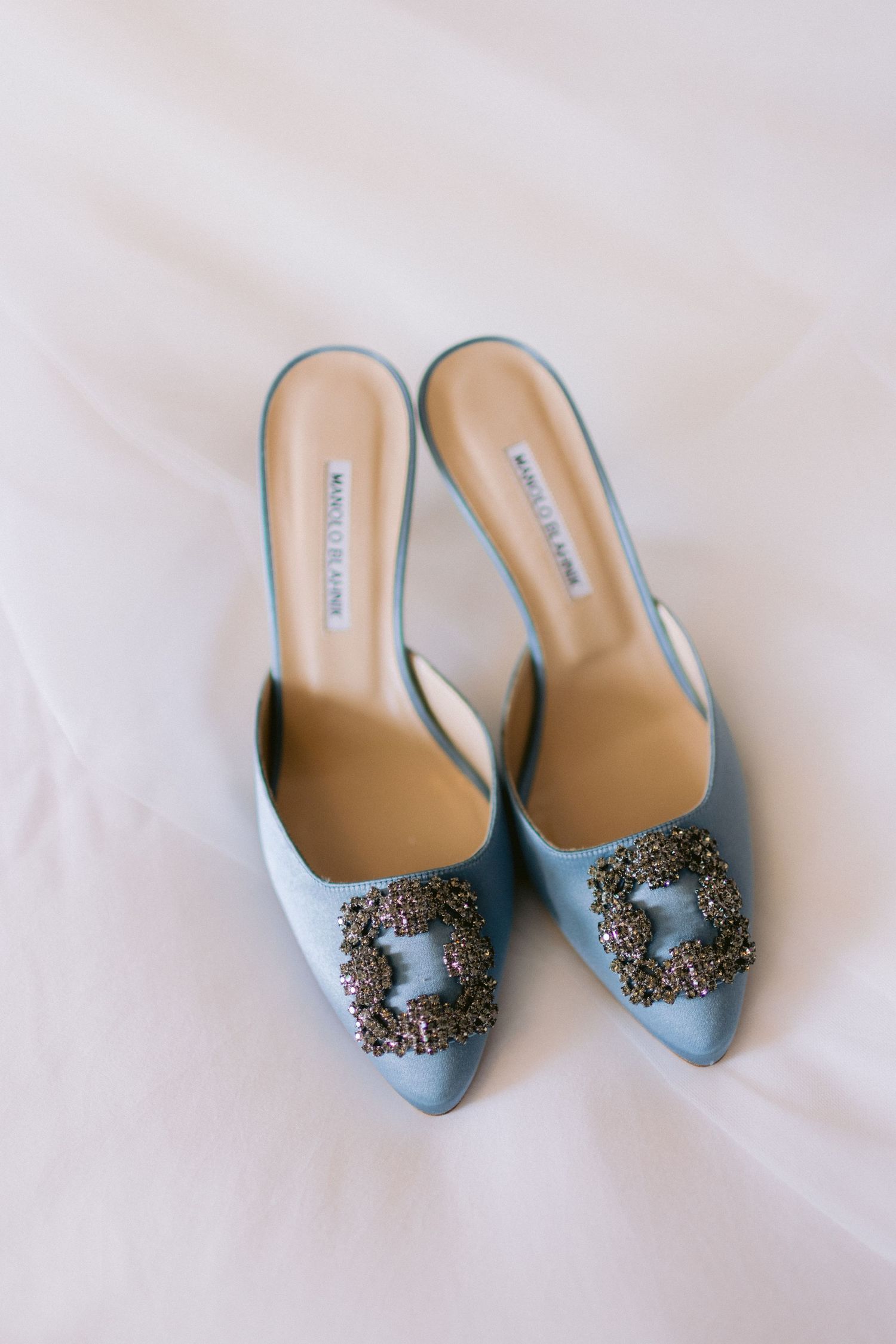 Light blue satin bridal shoes with ornate crystal embellishments displayed on white background.