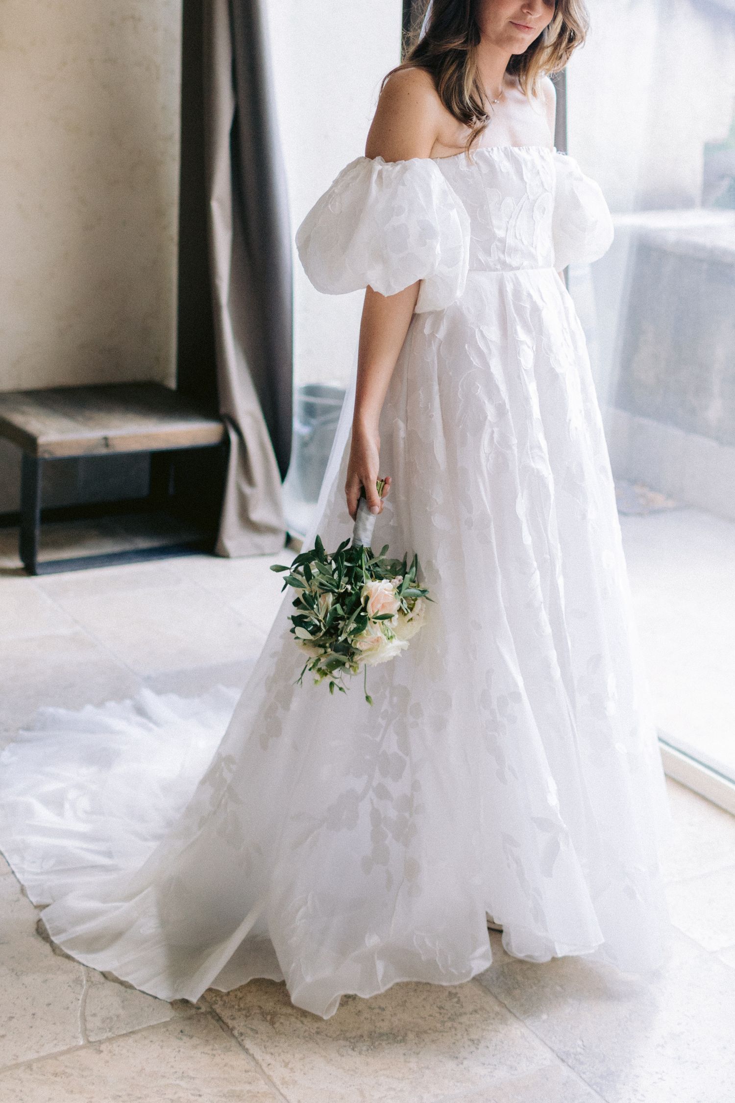 White wedding dress with flowing fabric and delicate details photographed in an elegant indoor setting.