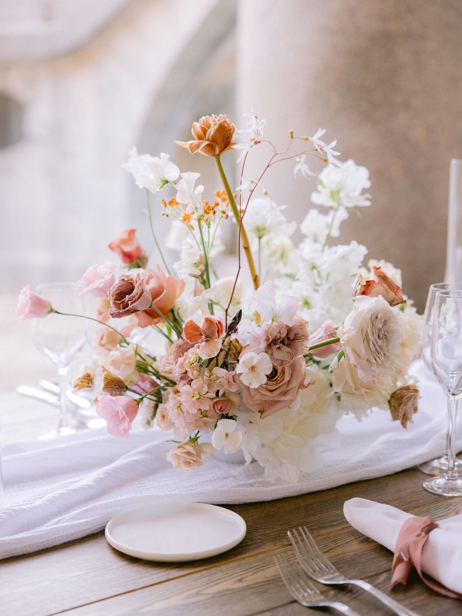 Romantic floral centerpiece with pink and white blooms on white tablecloth.