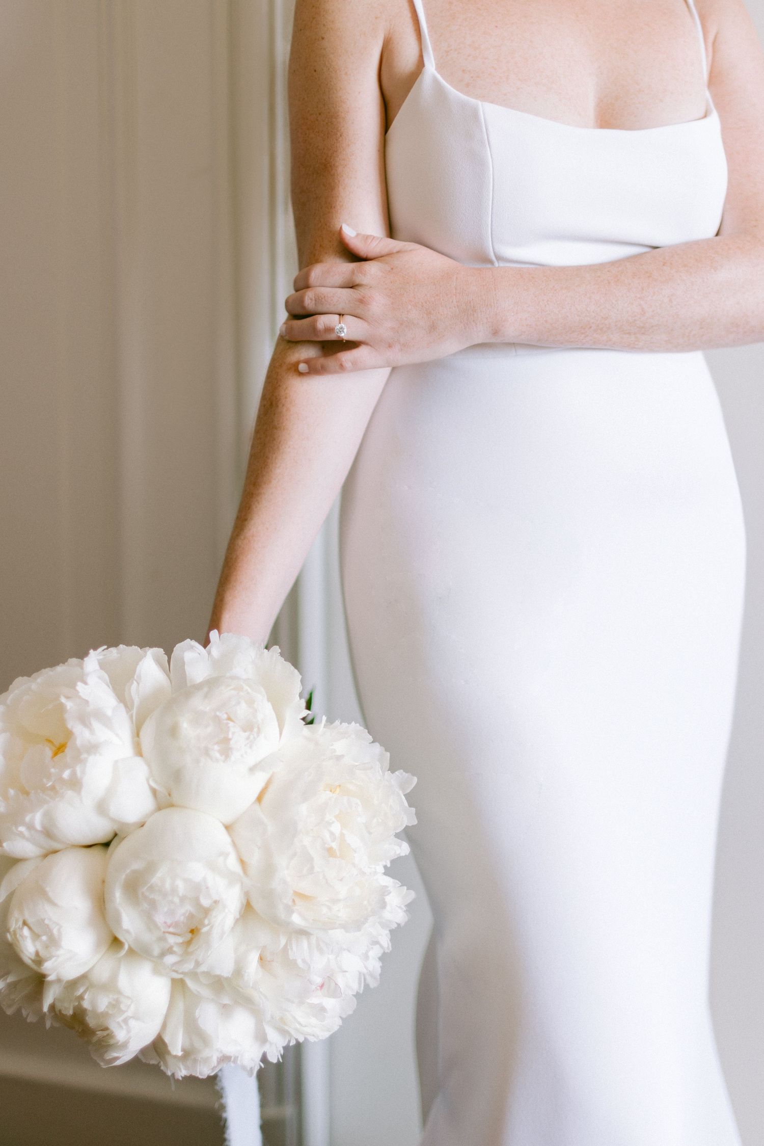 Close-up of white wedding dress and peony bouquet showing elegant bridal details.