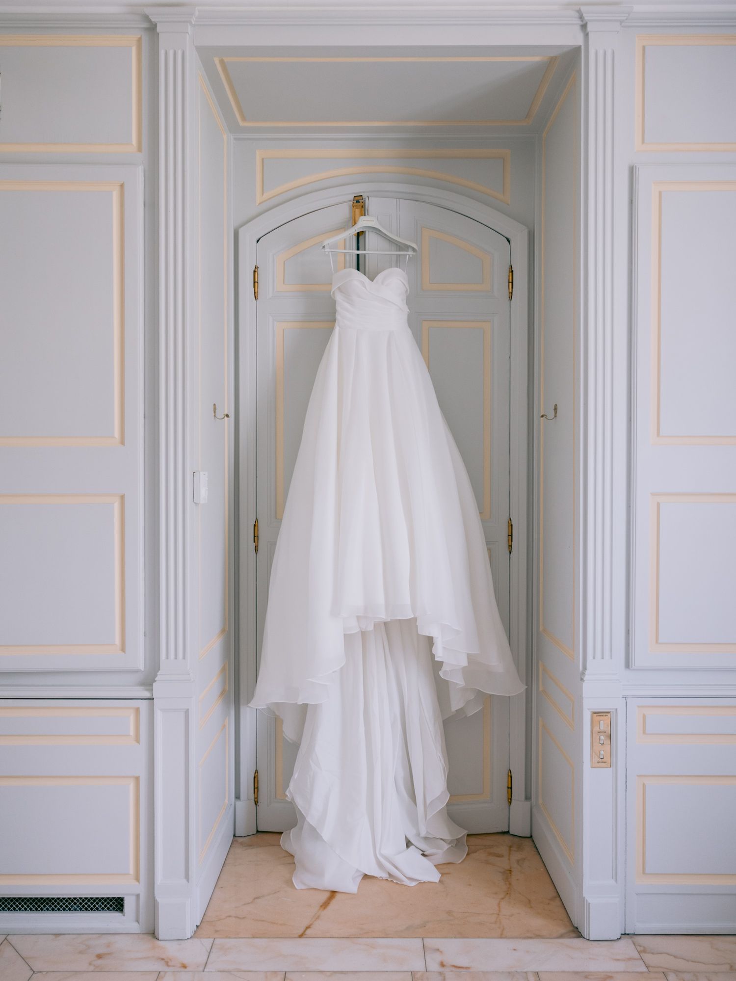 Wedding gown hanging in an elegant corridor with classic architectural details and gold trim.