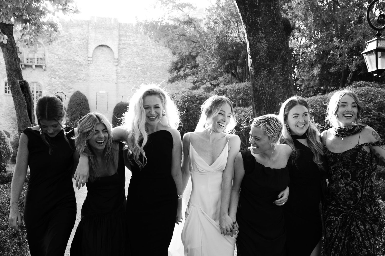 Wedding party members gather for black and white portraits against stone wall backdrop.