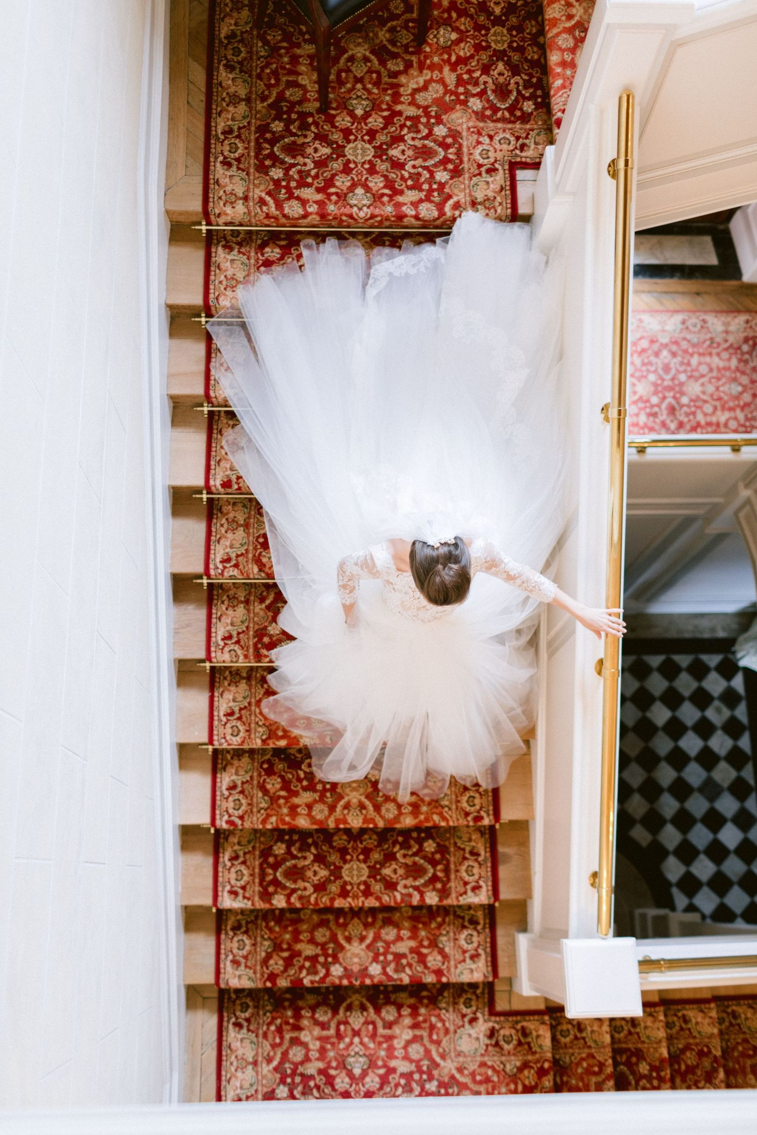 White tulle wedding dress displayed on ornate red wallpapered staircase.