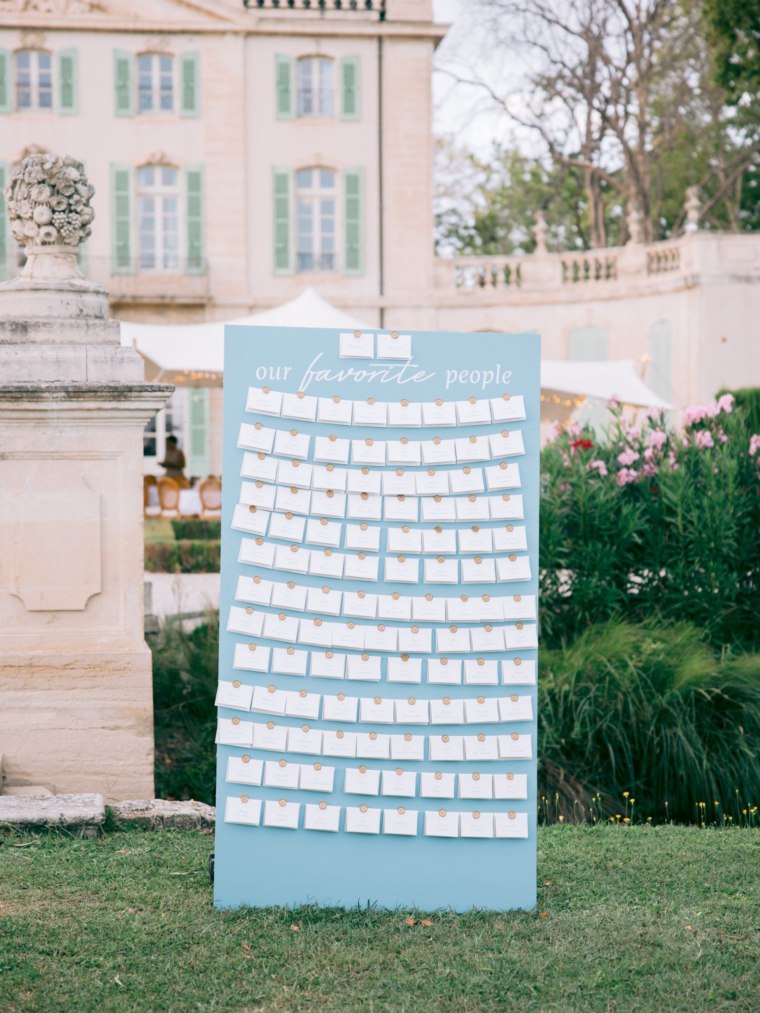 A light blue seating chart display board stands in front of a historic mansion.