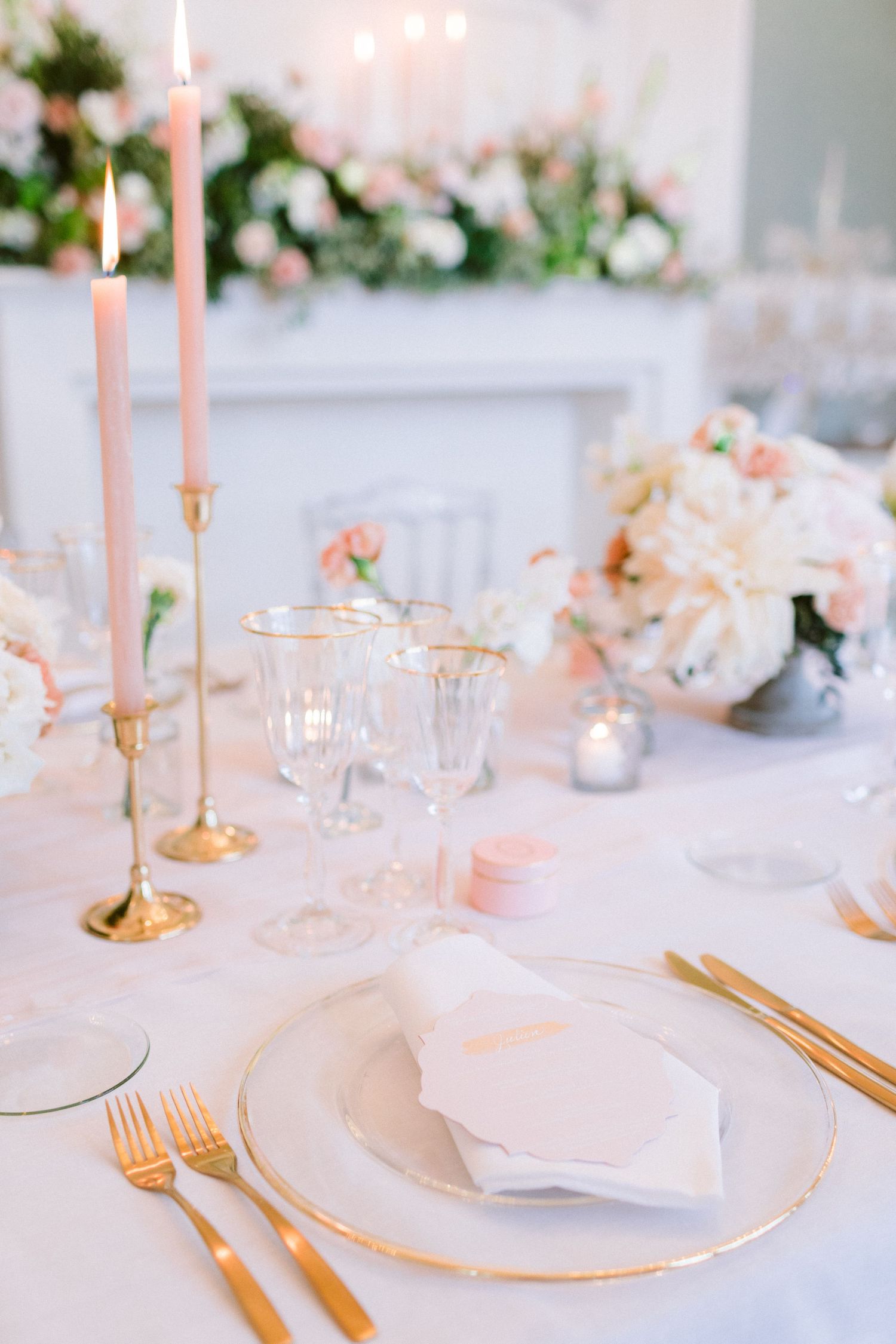 Elegant table setting with pink candles, gold cutlery, and white plates for a wedding reception.