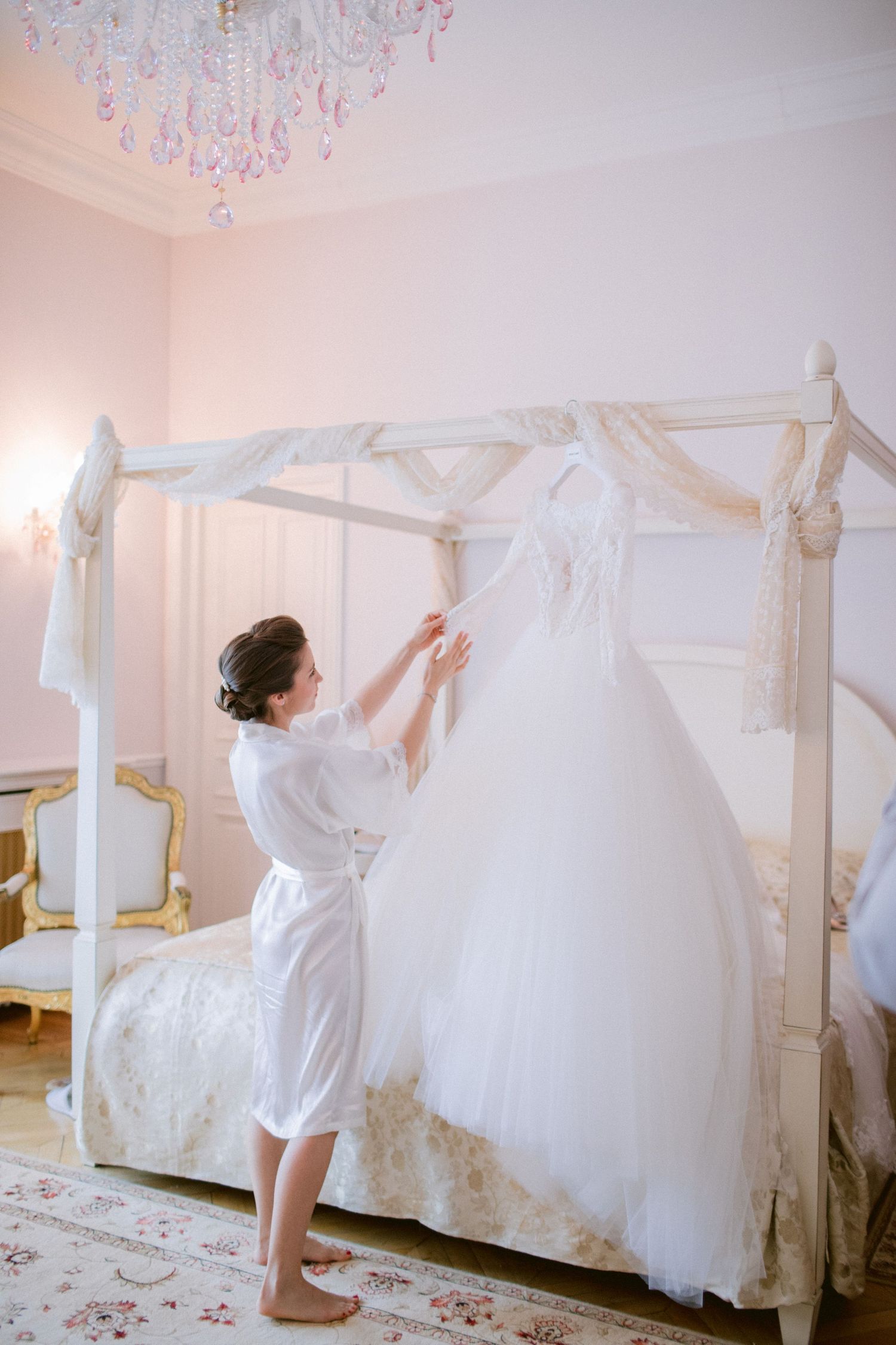 White wedding dress hanging on display in an elegant room with pink walls and ornate details.