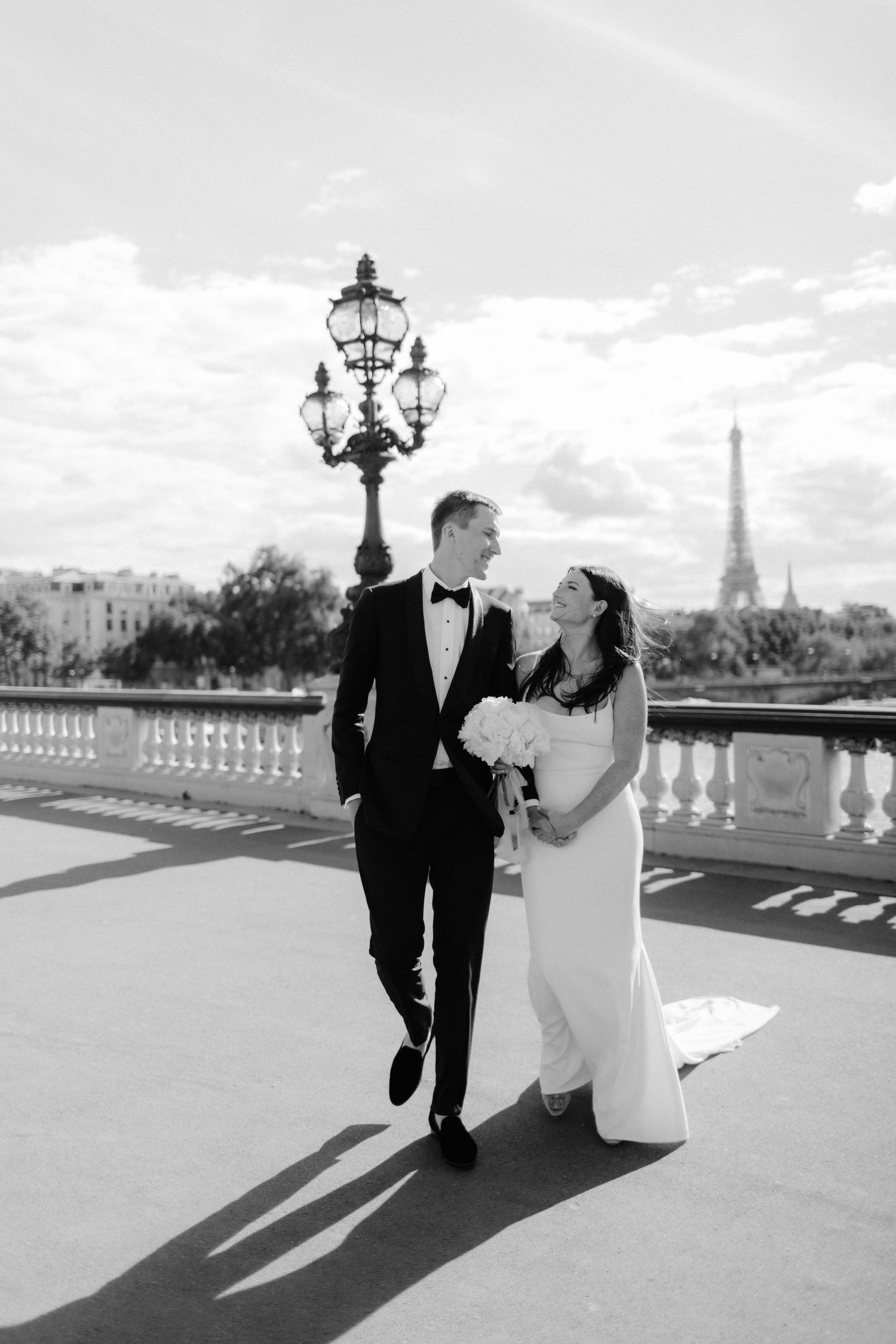 A couple walks along a balcony with the Eiffel Tower visible in the Paris skyline.