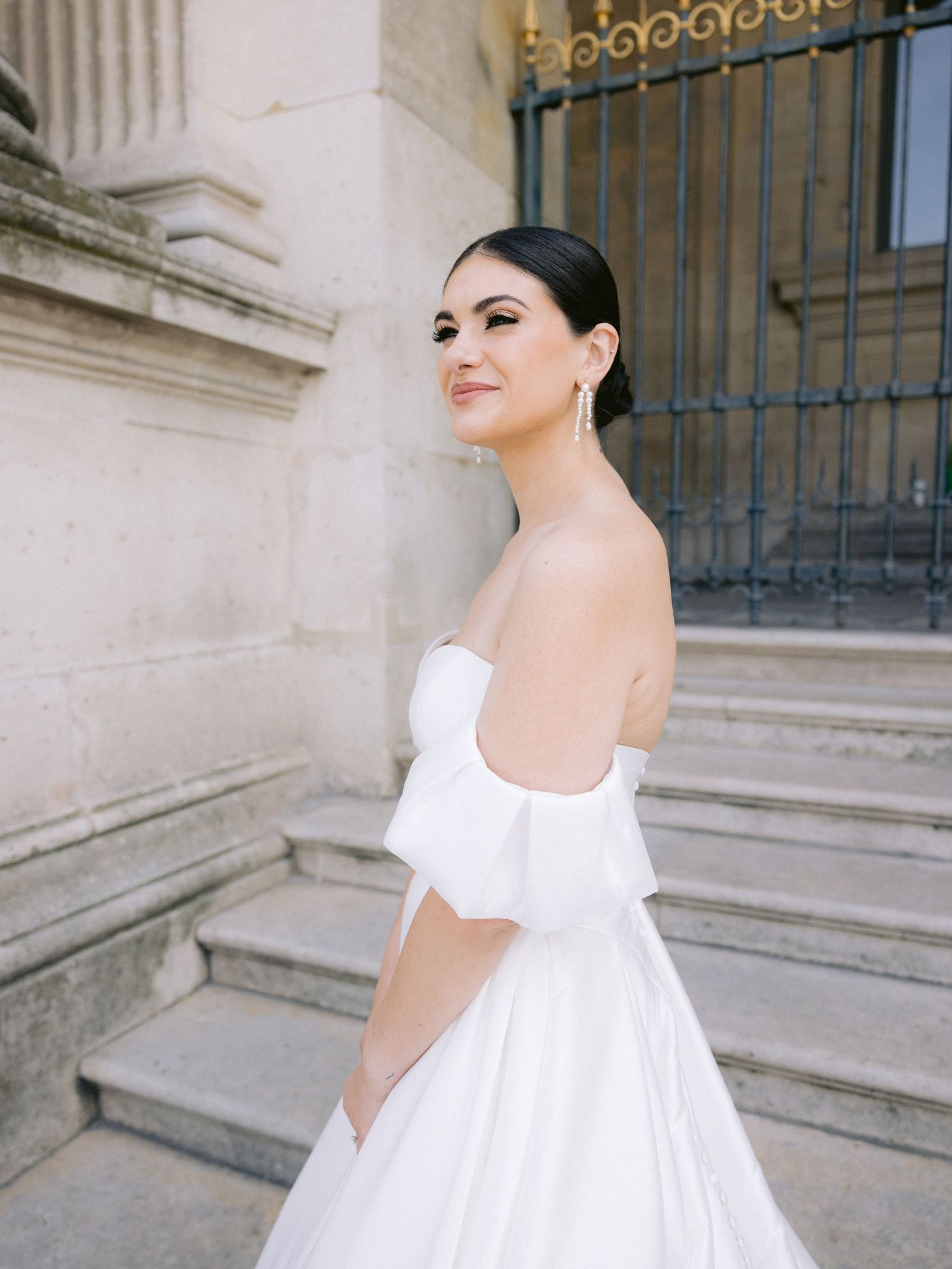 Elegant off-shoulder wedding gown photographed on stone steps with classical architecture.