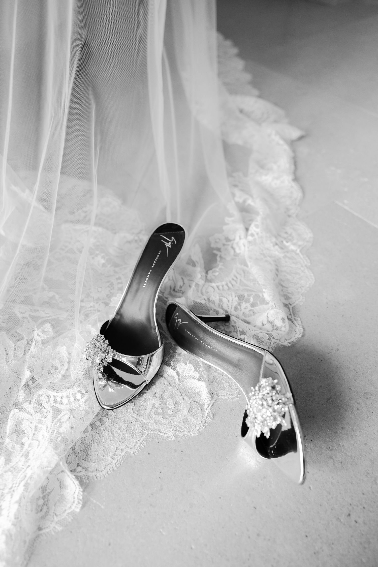 Artistic black and white detail shot of bridal shoes and lace wedding dress hem.