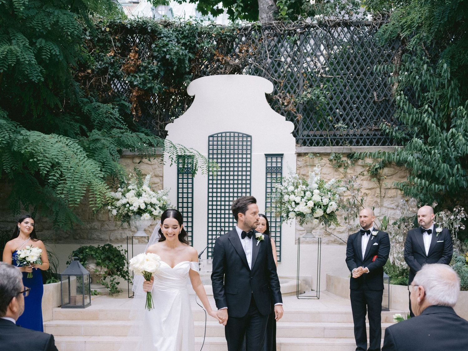 Outdoor wedding ceremony setup with white chairs arranged in rows amidst lush garden greenery.