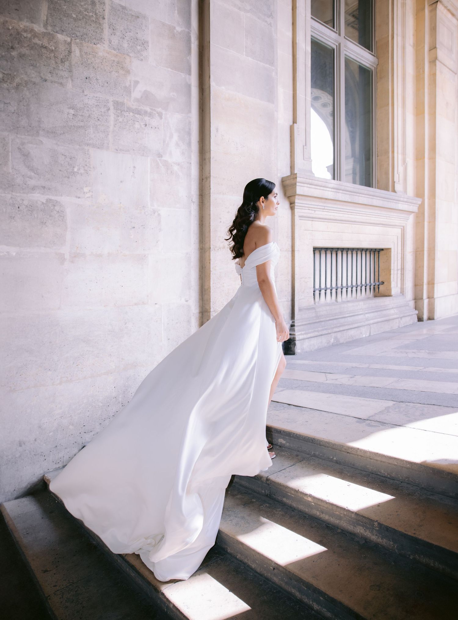 A flowing white wedding dress twirls in motion against a bright architectural backdrop.