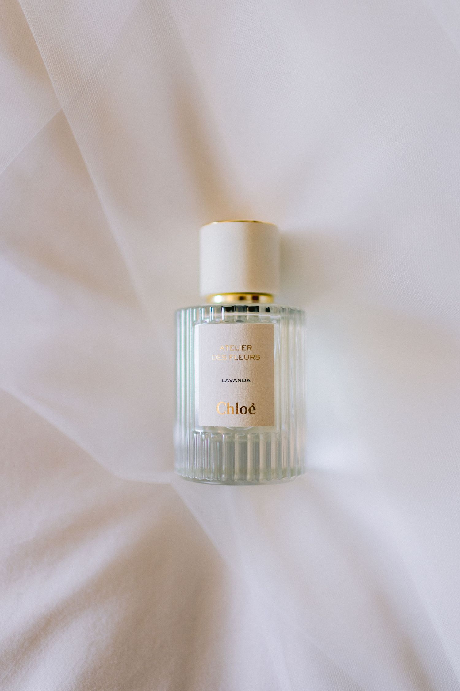 Elegant glass perfume bottle with ribbed design and gold cap on white background.