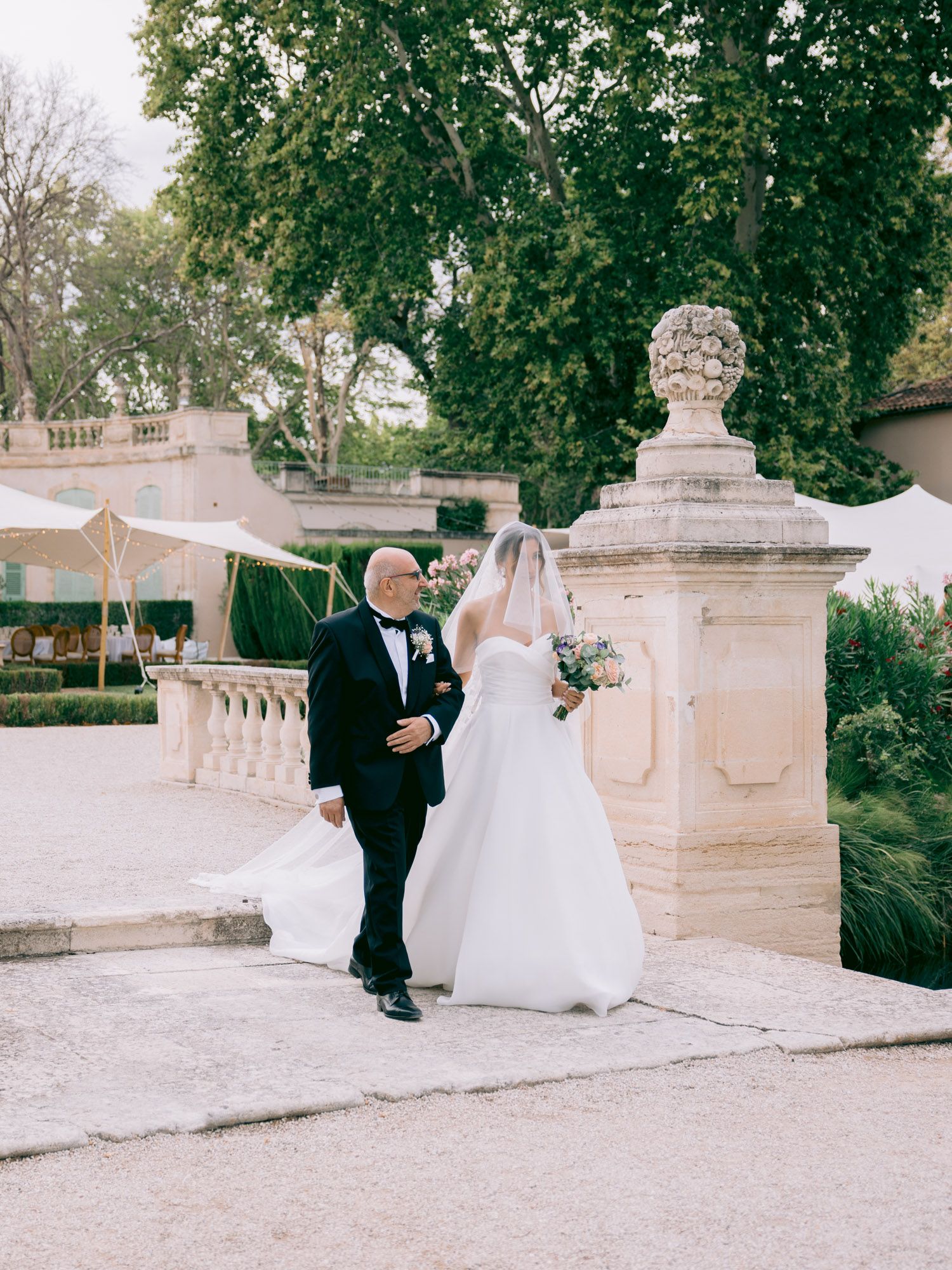 A wedding ceremony takes place on an elegant stone terrace with classical architectural details and lush greenery.