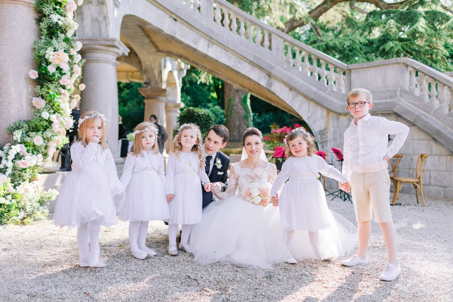 Wedding party in white dresses sitting on grand stone staircase outdoors.