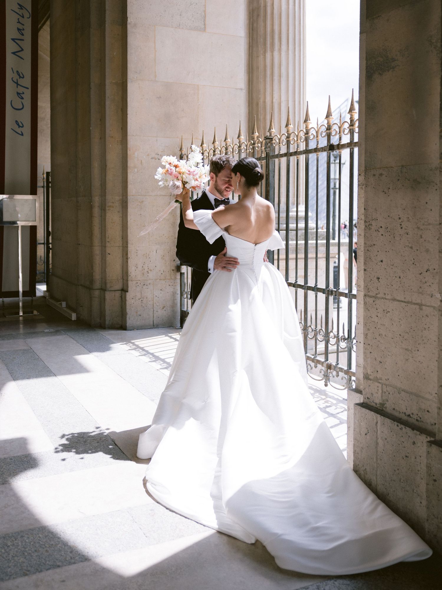 Romantic wedding moment captured in sunlit classical architecture setting.