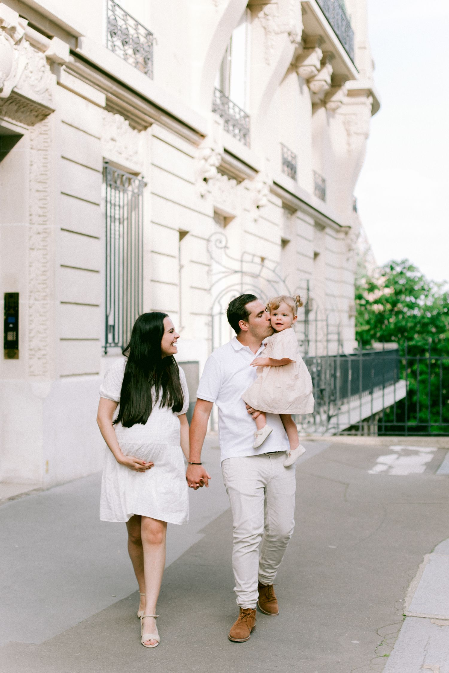 People in white outfits walking and posing along an elegant building exterior.