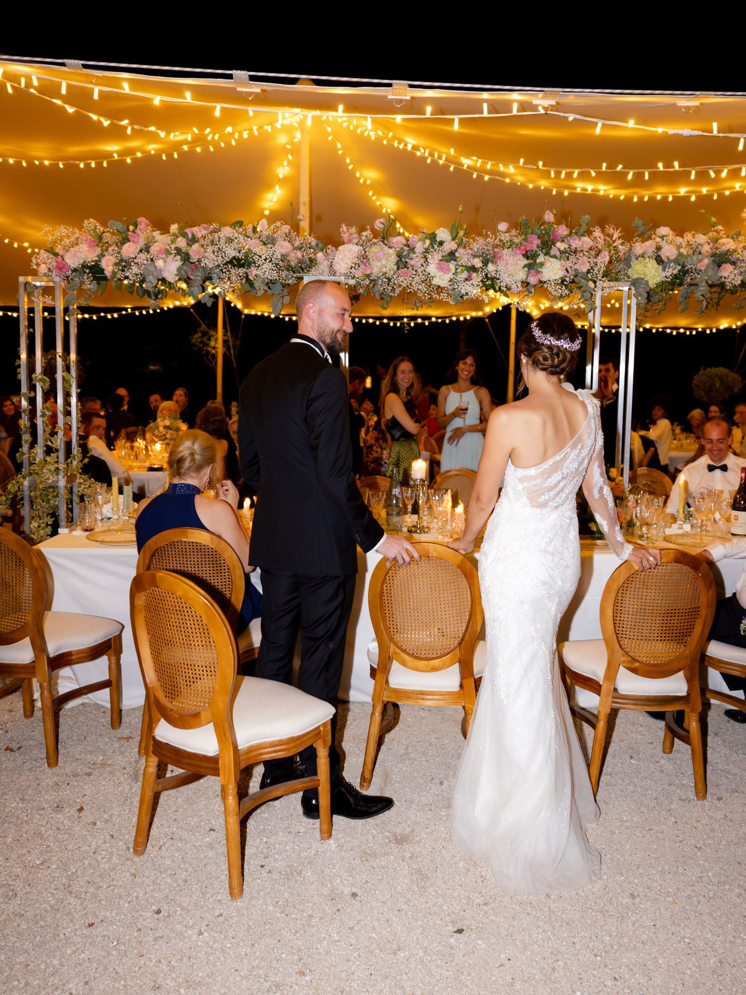 An elegant wedding reception under string lights with floral decorations and formal table settings.
