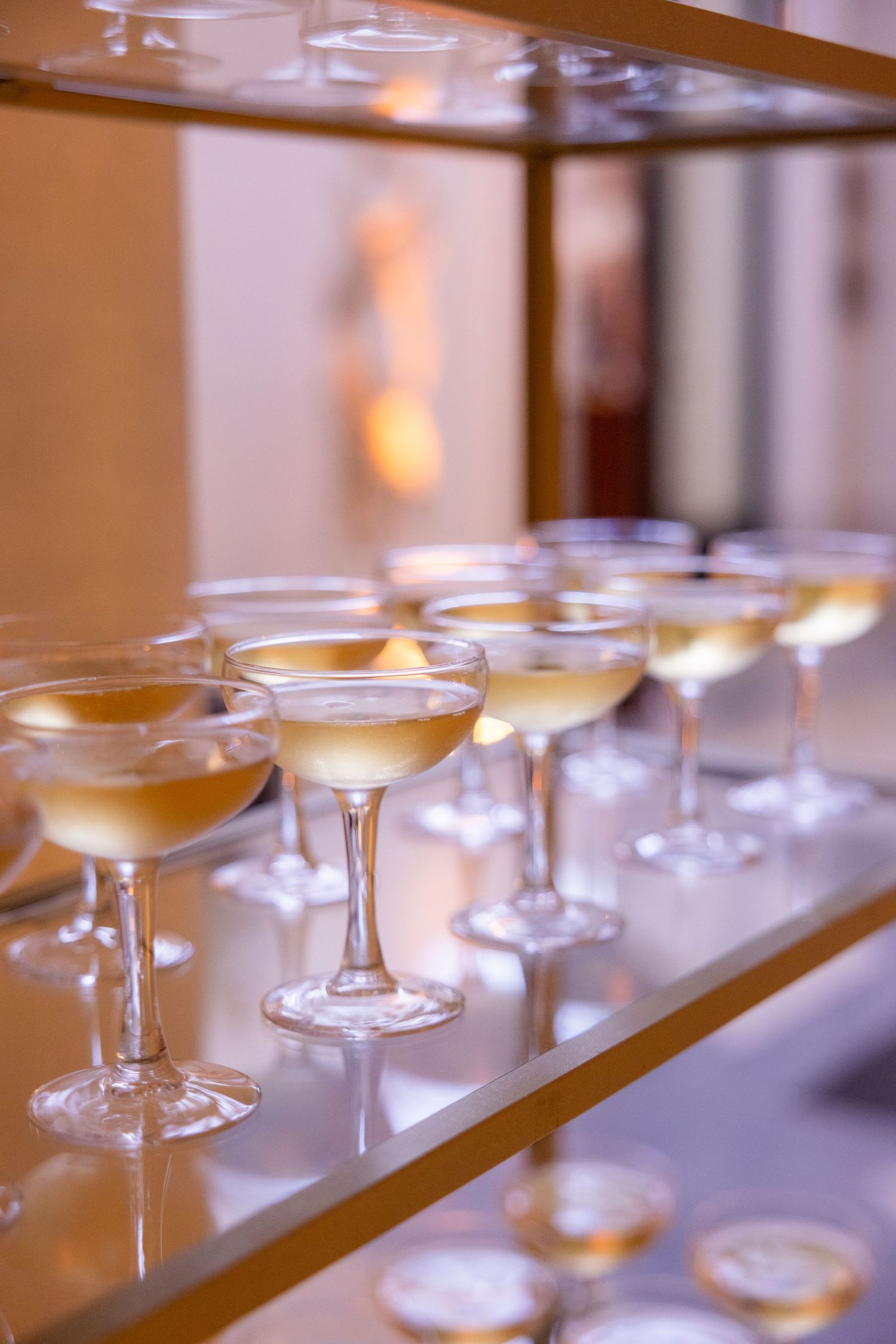 Elegant champagne glasses lined up on a wooden bar surface at a wedding reception.