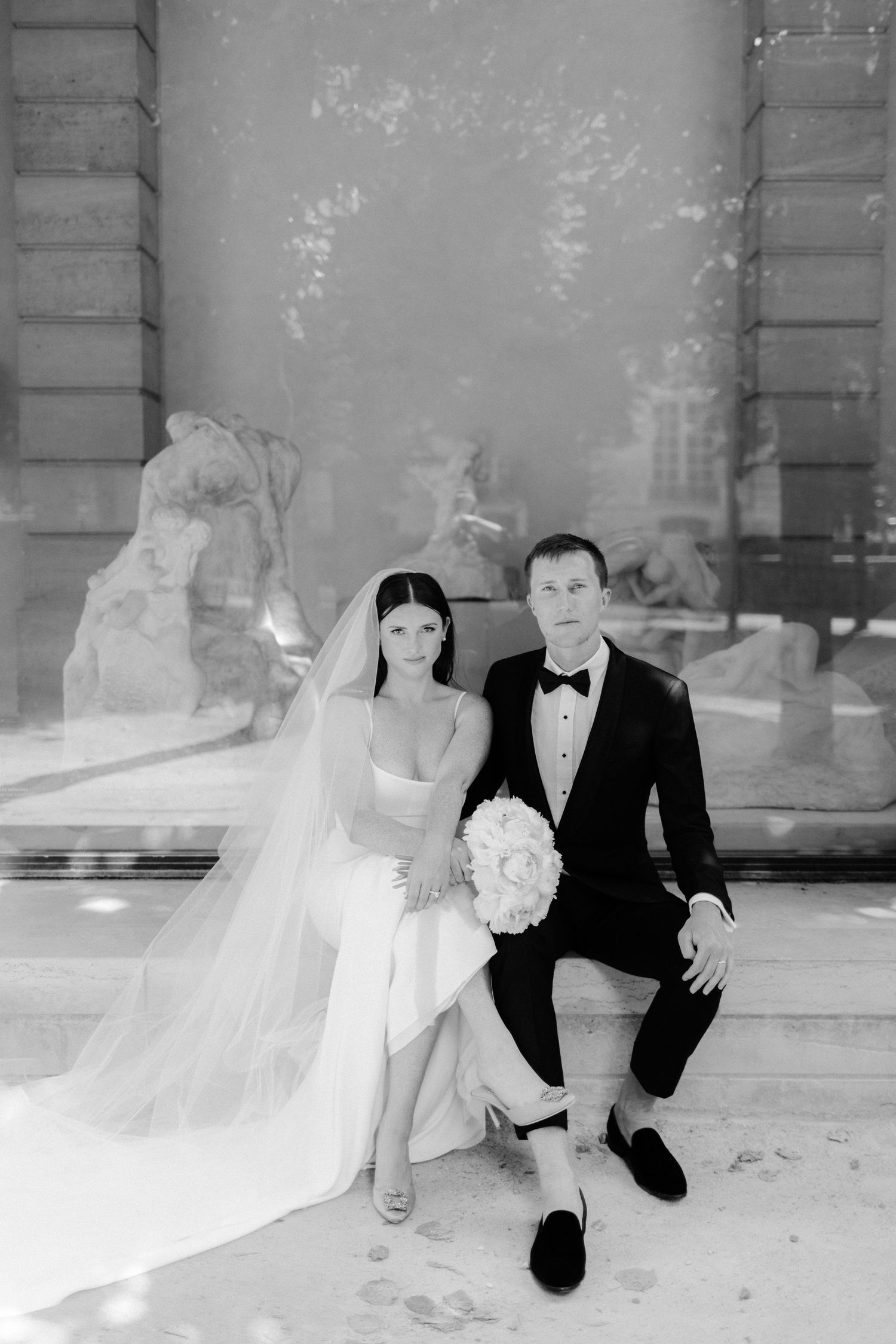 A couple in formal wedding attire posing against an elegant architectural backdrop.