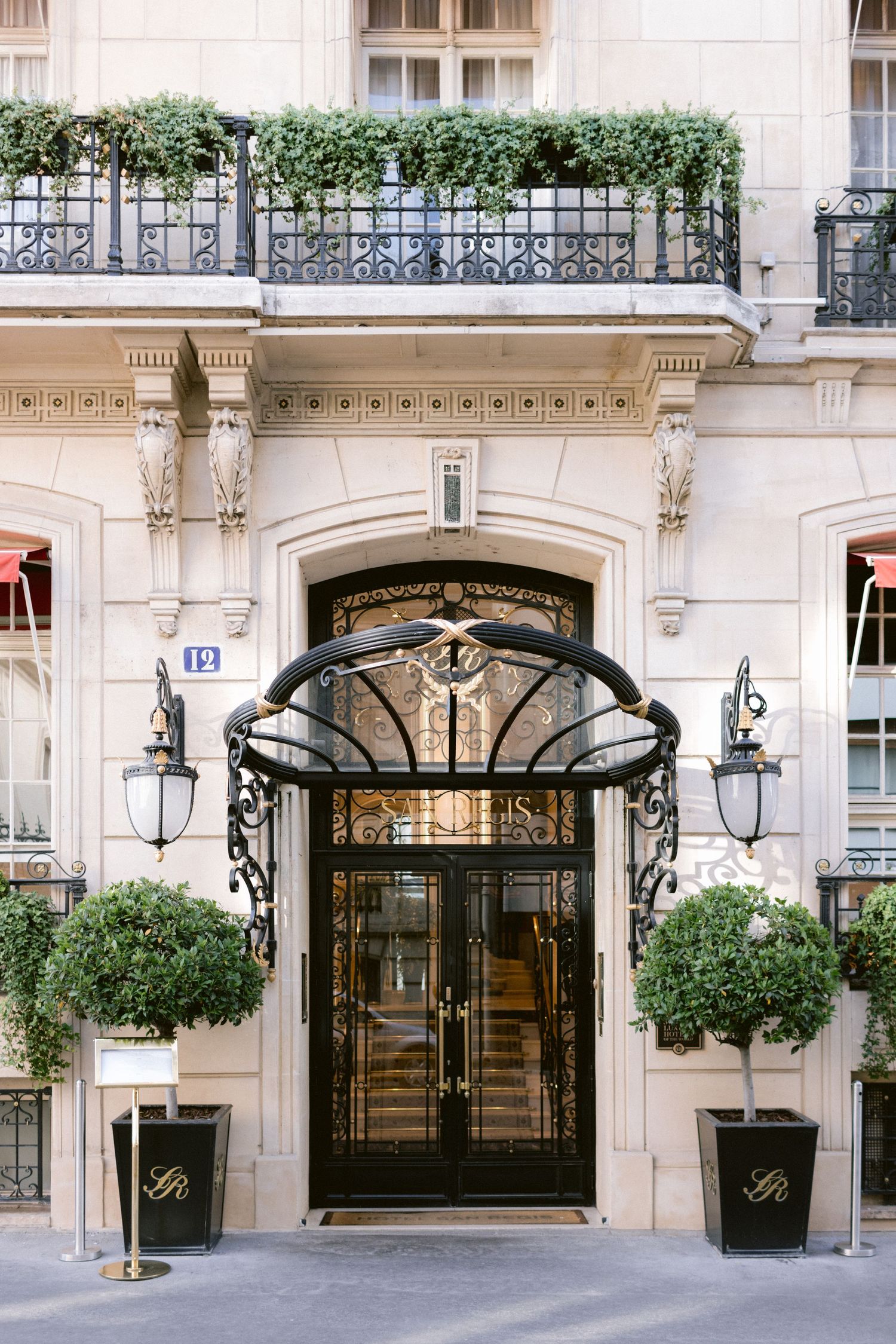 Elegant entrance to a luxury Parisian hotel with ornate iron and glass details.